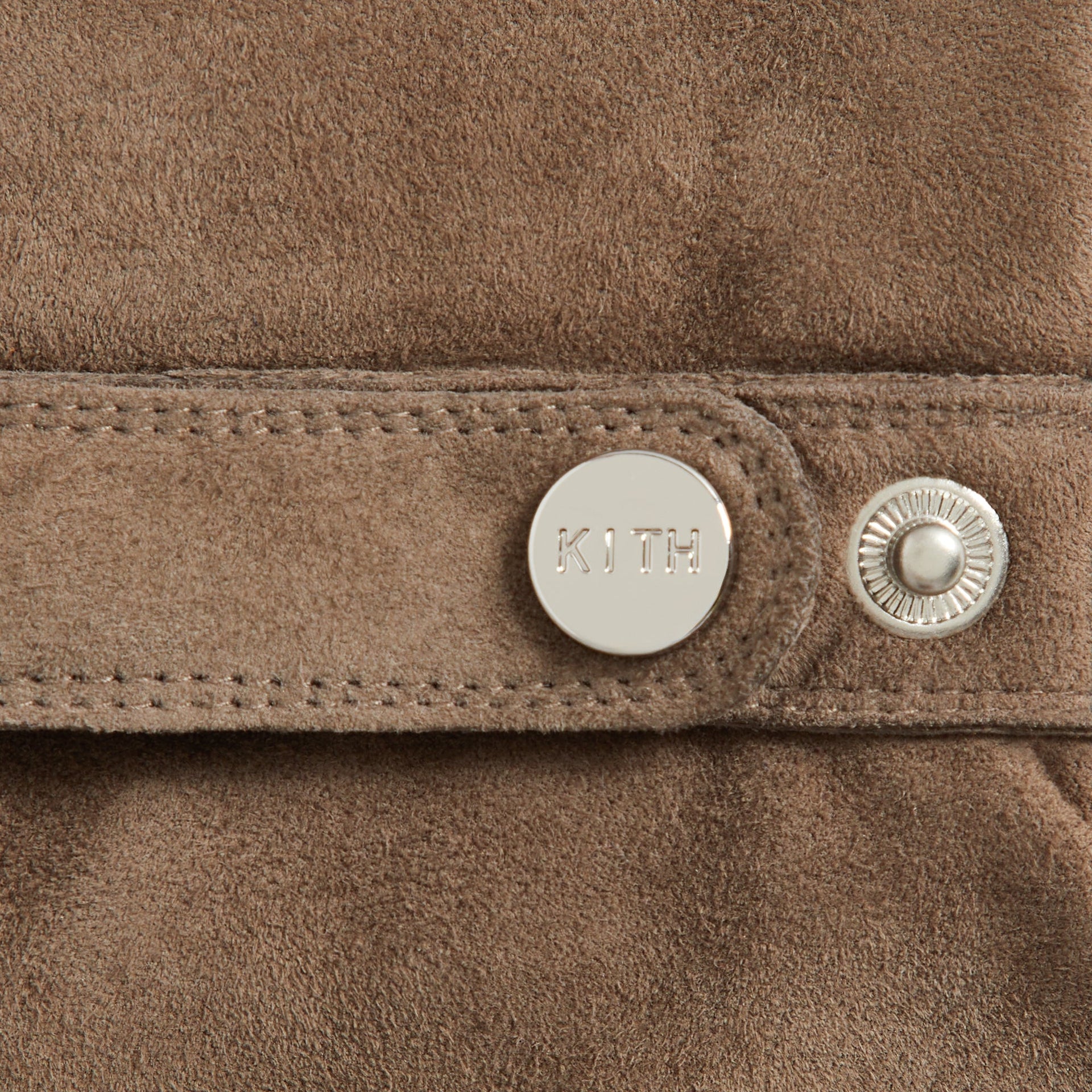 Close-up detail of Kith Suede Manhattan Gloves in Java showing engraved KITH snap button and stitched strap
