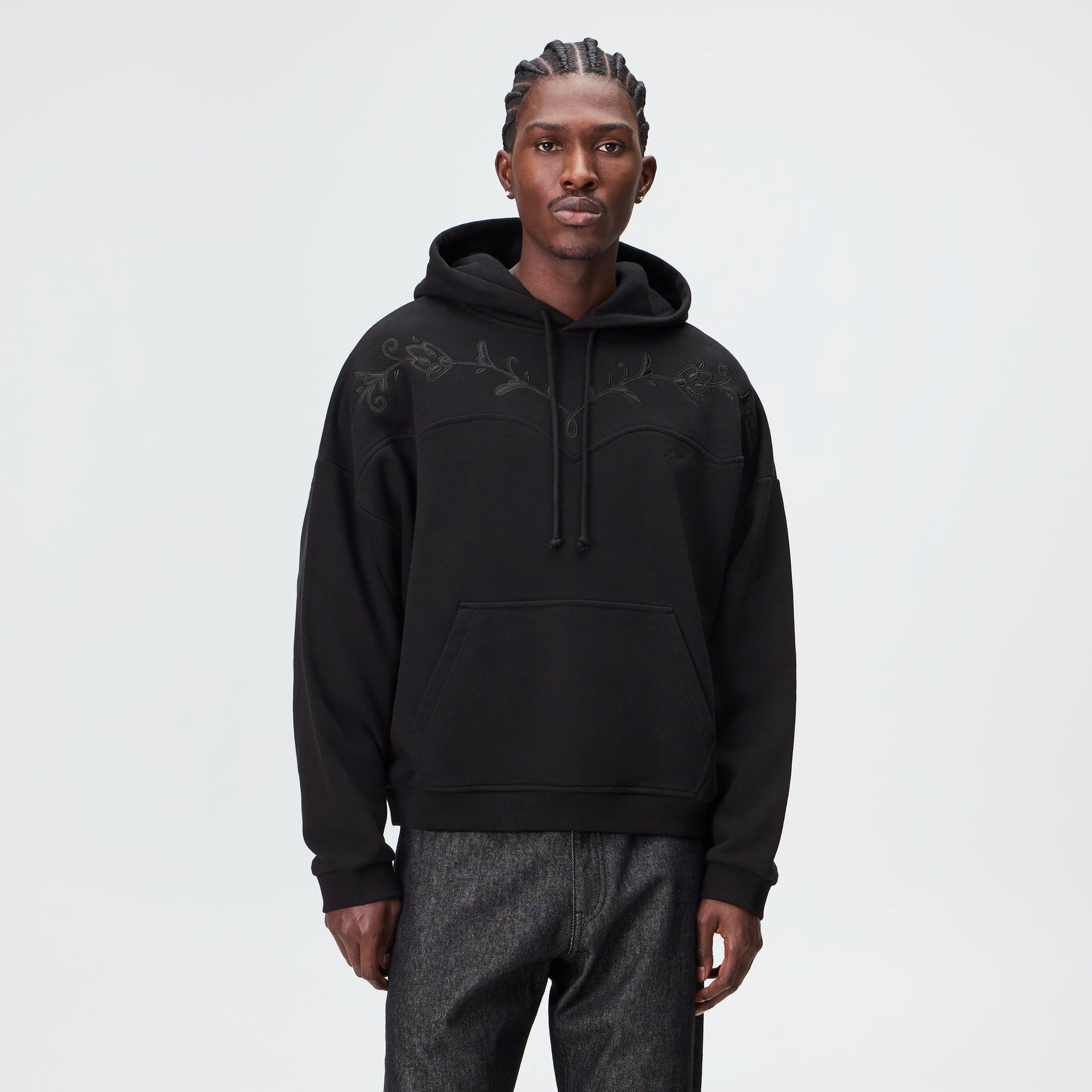 Man wearing the Kith Heritage Filigree Braxton hoodie in black with tonal floral embroidery, front view