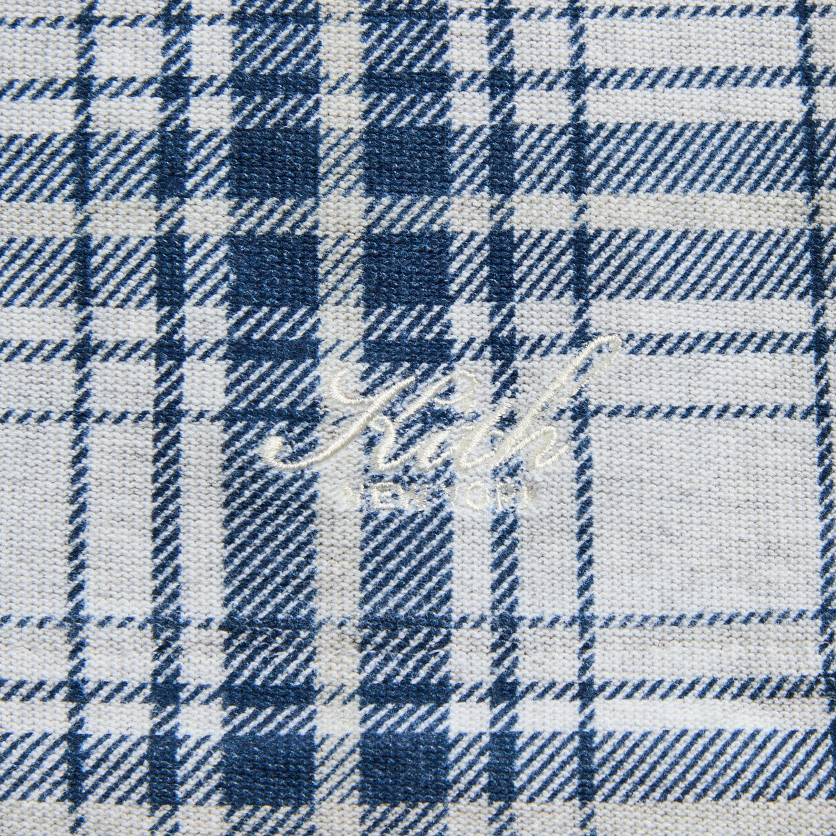 Close-up of the white 'Kith' script on the blue plaid Kurt quarter-zip