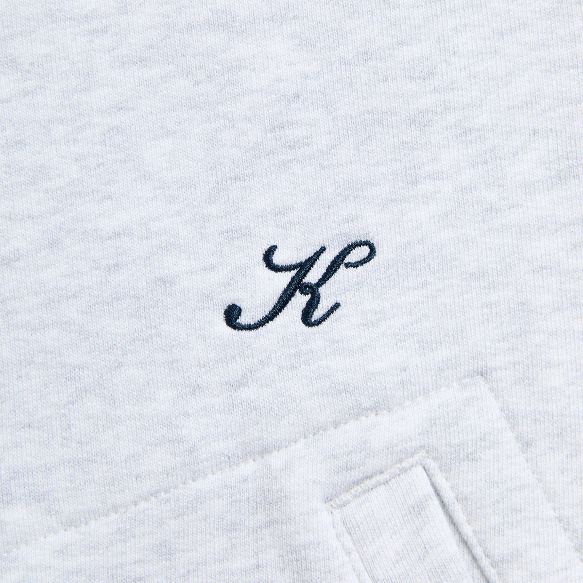 Close-up of the navy K script monogram on the light grey Khenny reversible hoodie