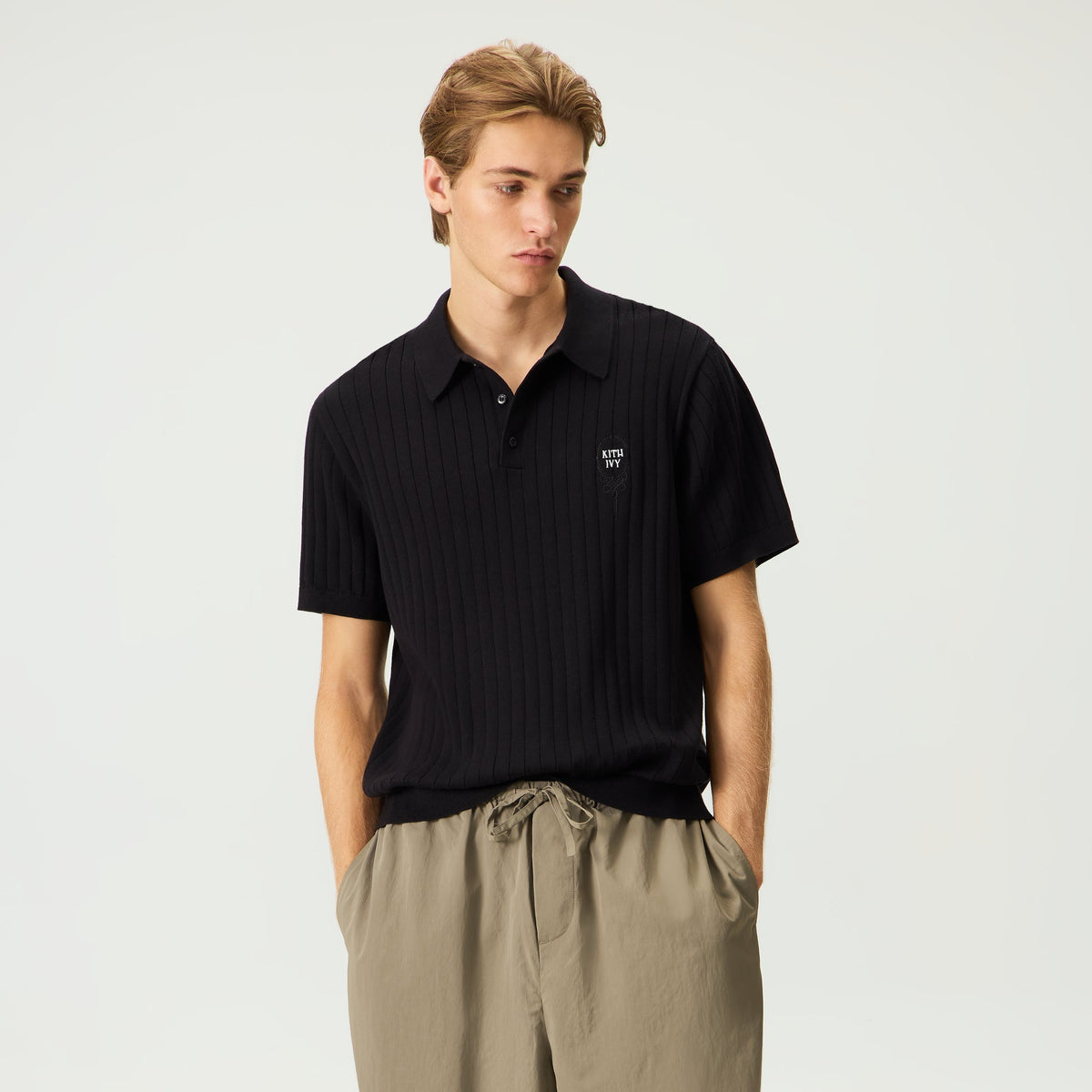 Model wearing black Kith Ivy Knit Tilden Polo with khaki drawstring pants, front view