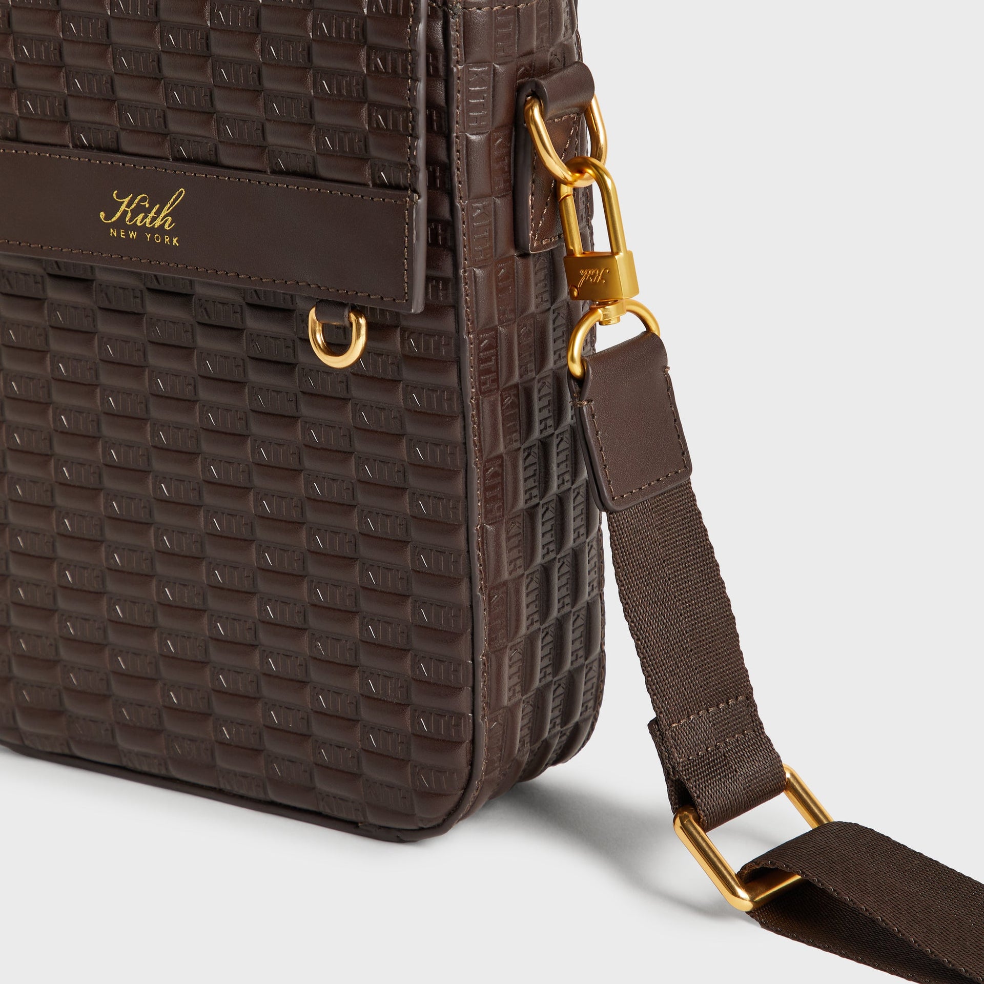Close-up side detail of the Kith Monogram Smooth Leather Explorer Pack showing gold-tone hardware clasps, D-ring, and leather pull tab on the strap