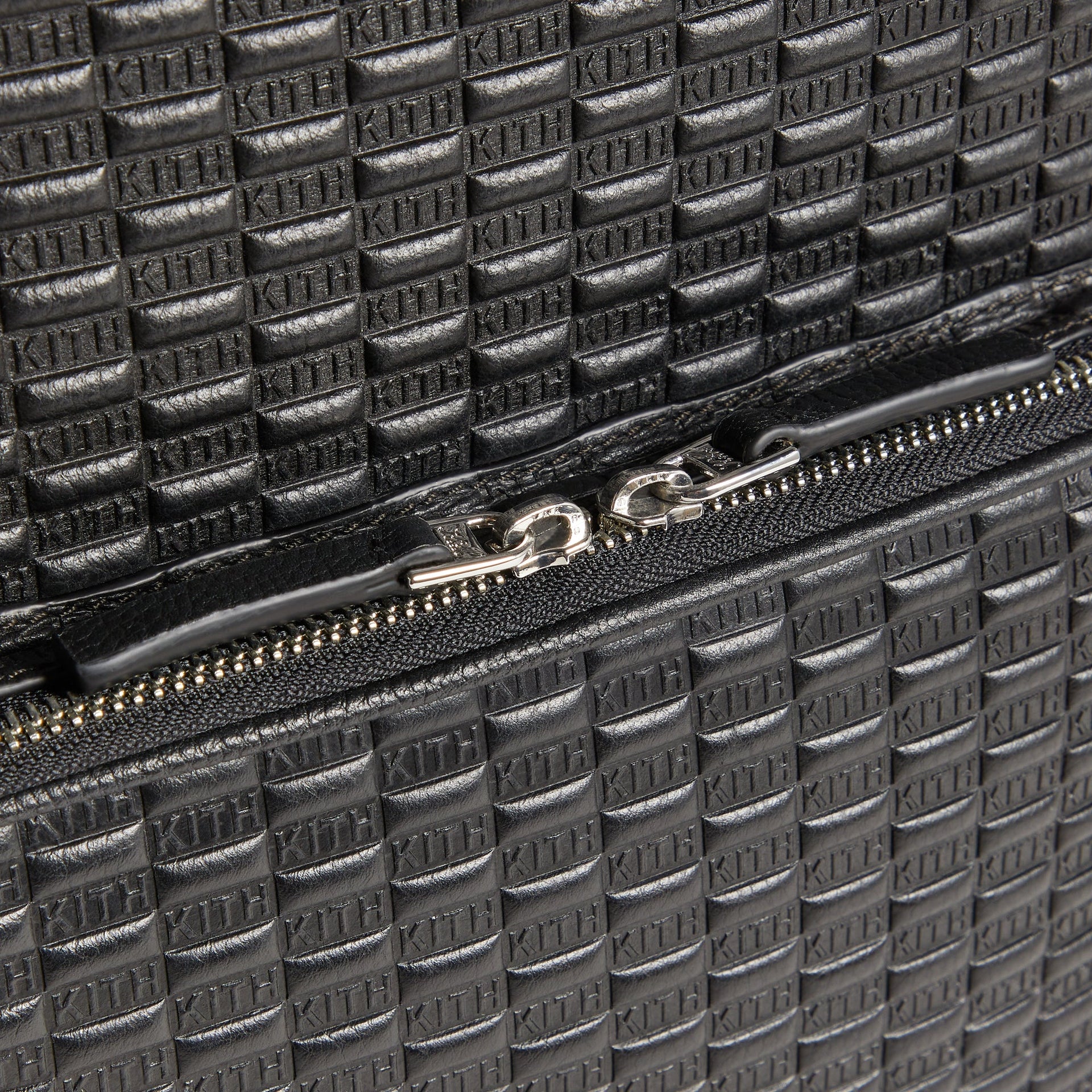 Close-up of the Kith Monogram Tumbled Leather Backpack's silver zipper pull with engraved K charm on the main compartment.