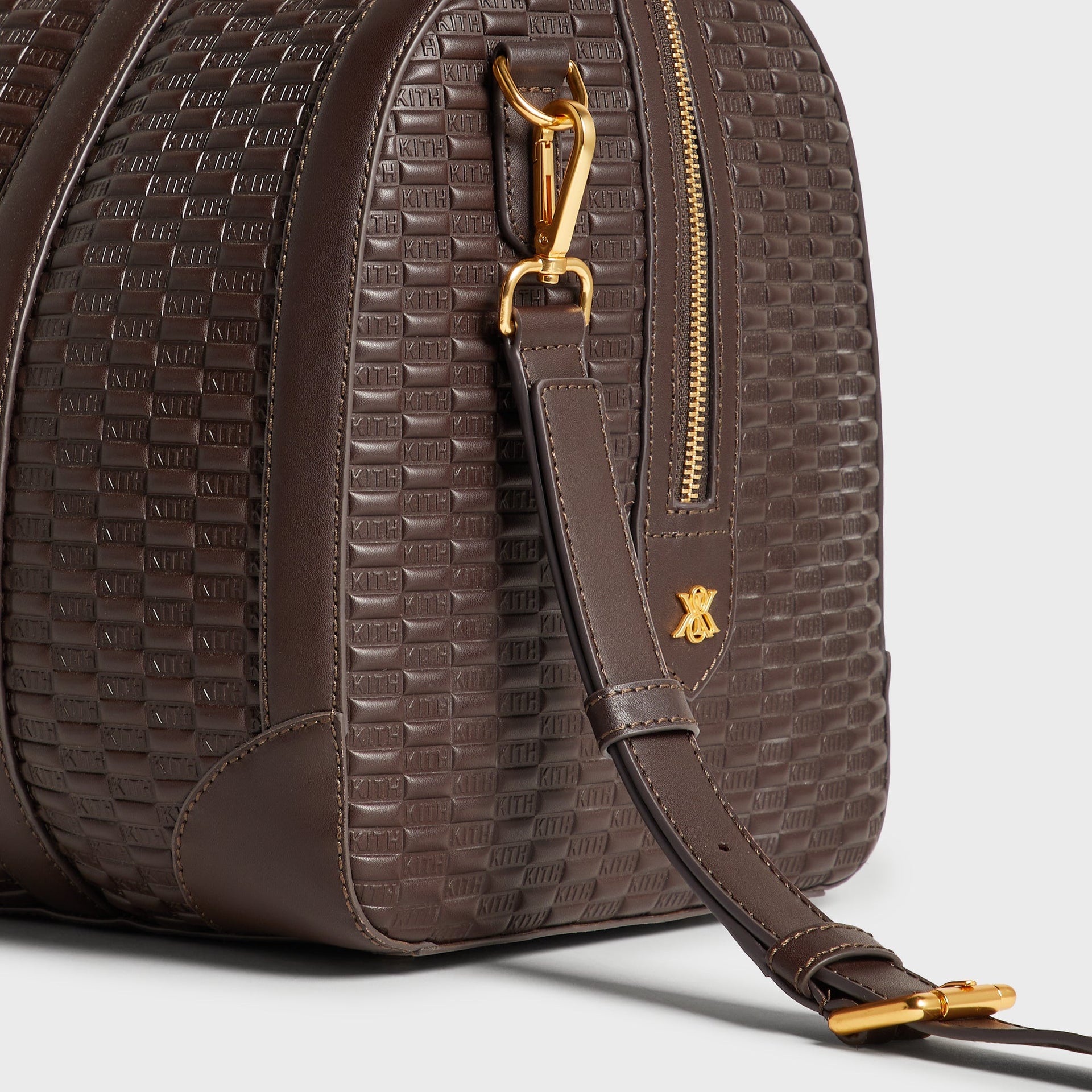 Detail of gold hardware, strap clip, and logo charm on the Kith Traveler K40 Duffle Bag