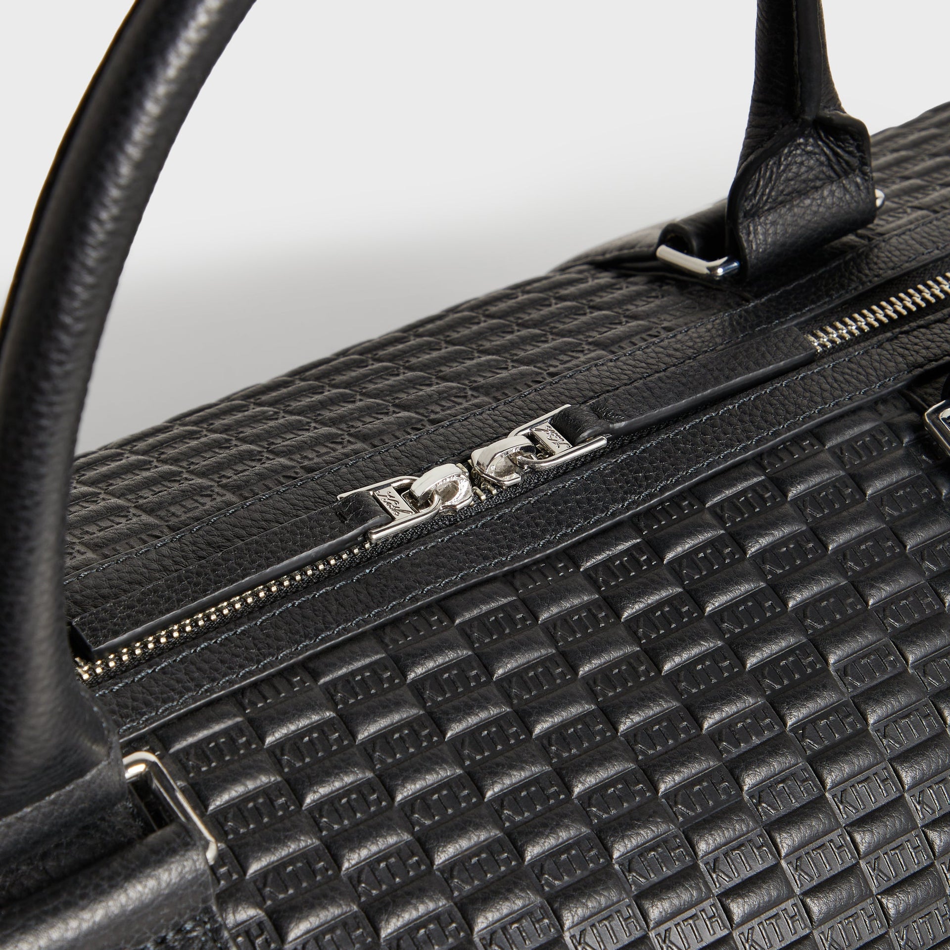 Close-up of the Kith Monogram Tumbled Leather Traveler K55 Duffle Bag's top handles and silver zipper pull with engraved K charm.