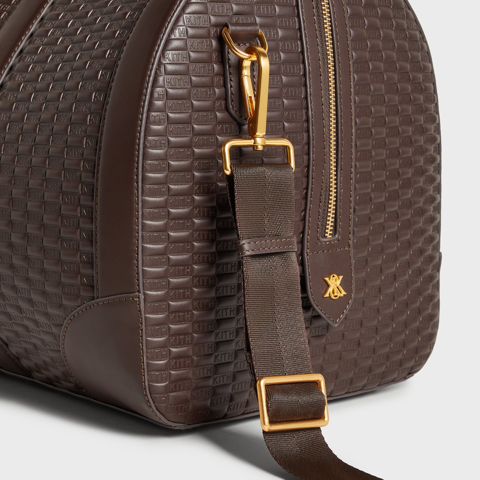 Detail of gold hardware, strap clip, and logo charm on the Kith Traveler K55 Duffle Bag