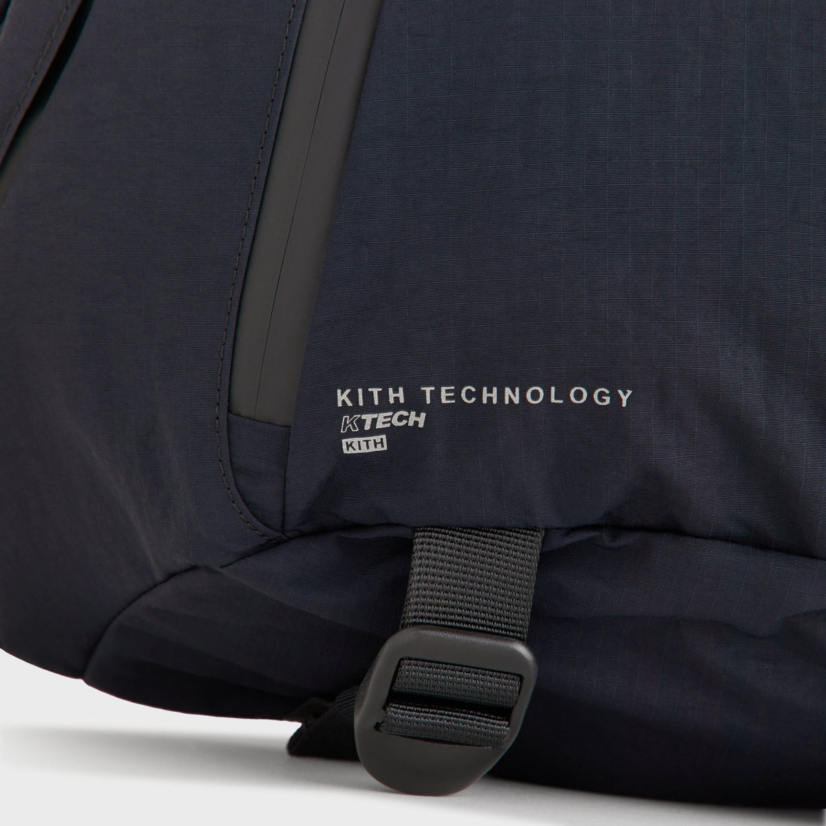 Close-up of the KITH TECHNOLOGY KTECH tag beside a zip pocket on the Sling Backpack