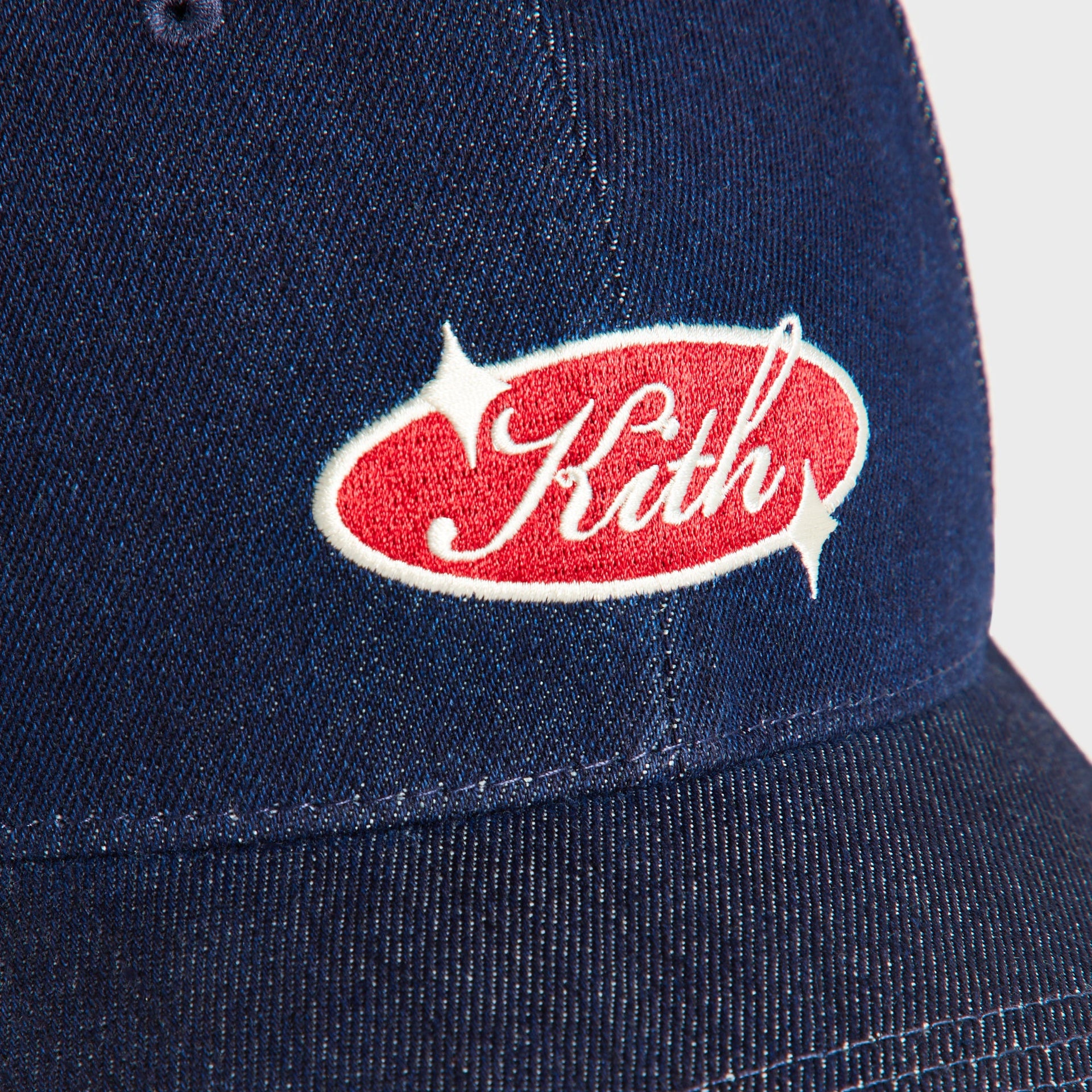 Close-up of the embroidered red and cream Kith oval logo patch on the Savin Wash denim cap