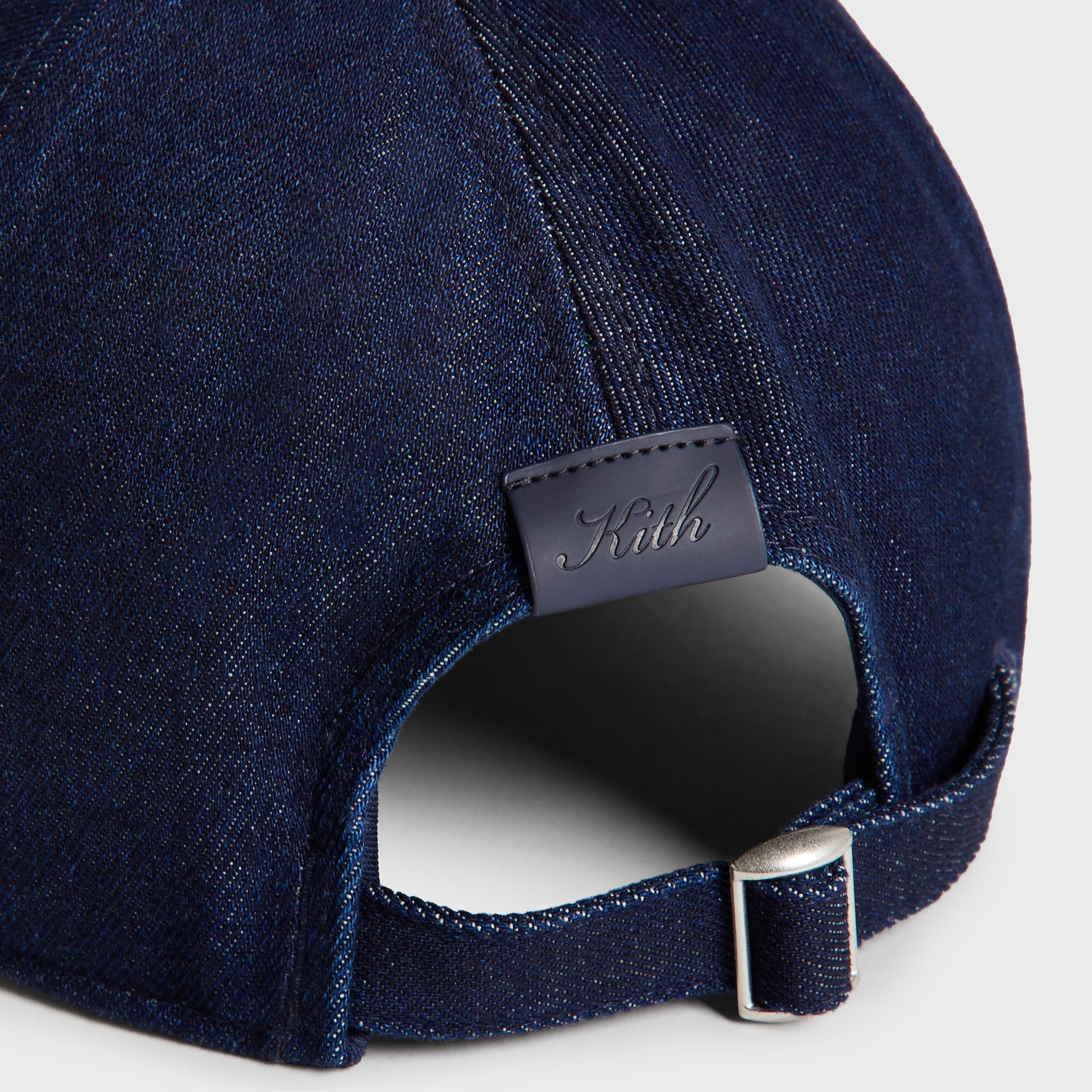 Close-up of the Kith Low Profile Raw Denim Classic Cap in Savin Wash back strap, showing the engraved Kith leather patch and adjustable metal buckle