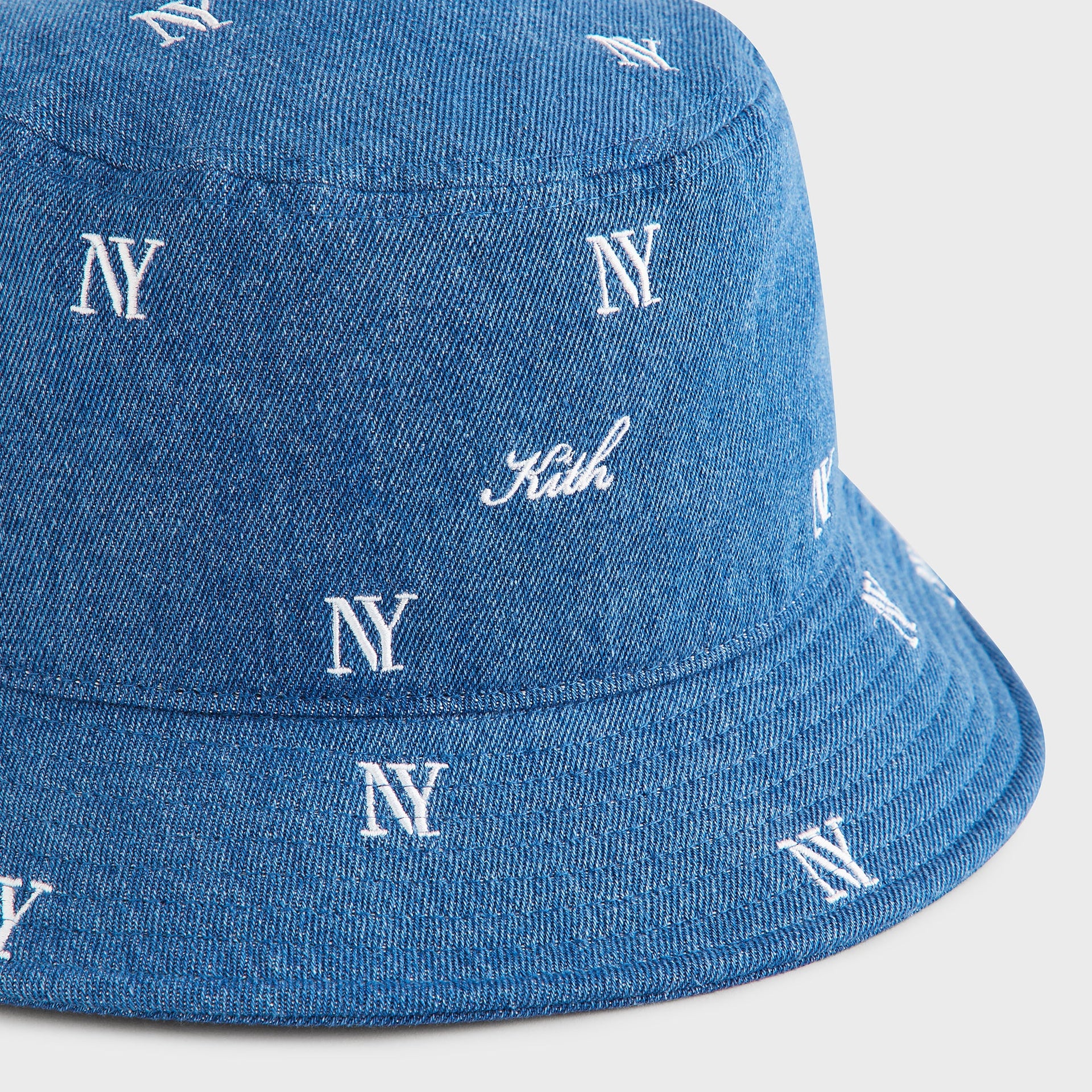 Kith NY All-Over Embroidery Dawson Bucket Hat in Medium Indigo, macro detail of Kith script and NY logo embroidery on denim