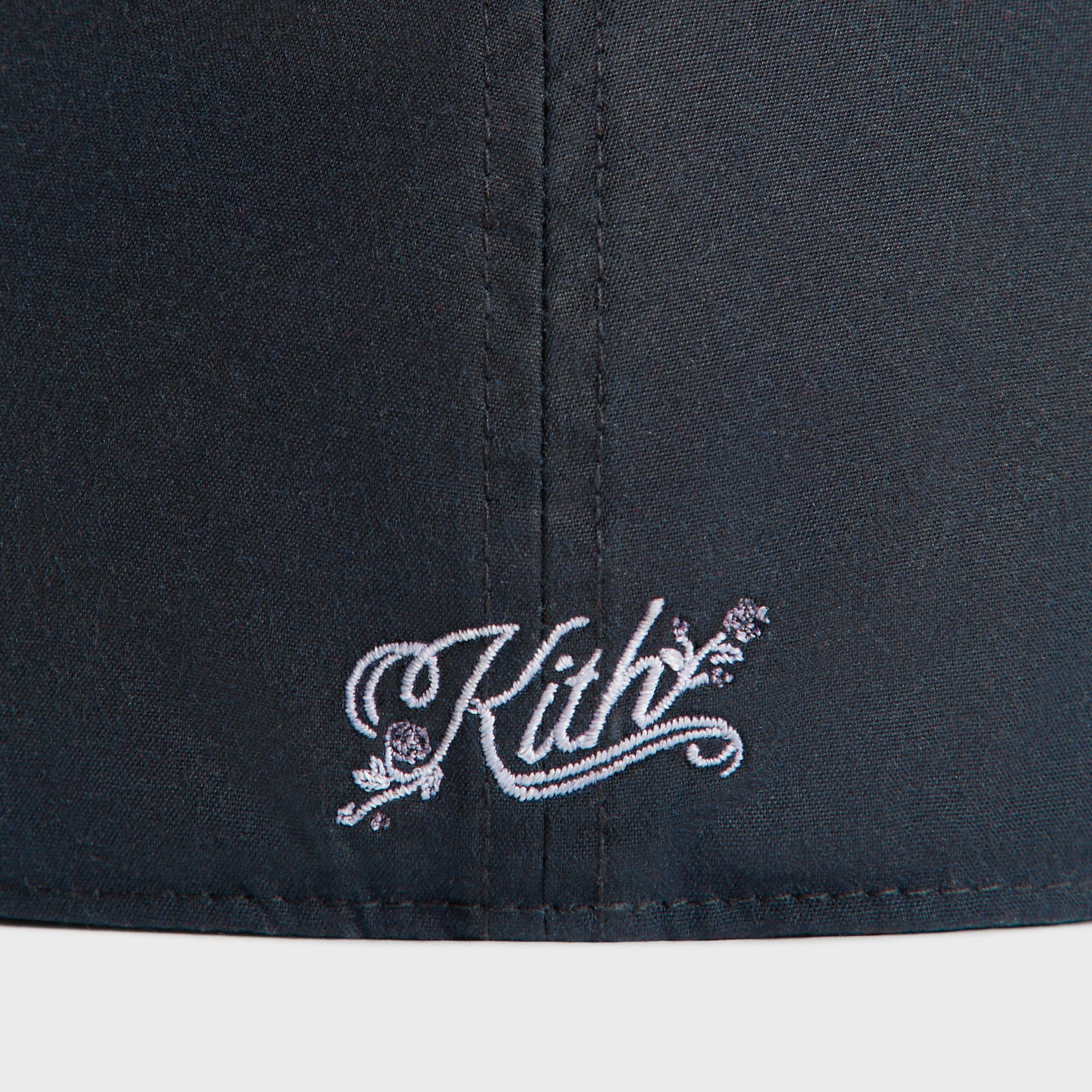 Close-up of the white Kith rose-script embroidery on the back of the navy Nocturnal Yankees cap.