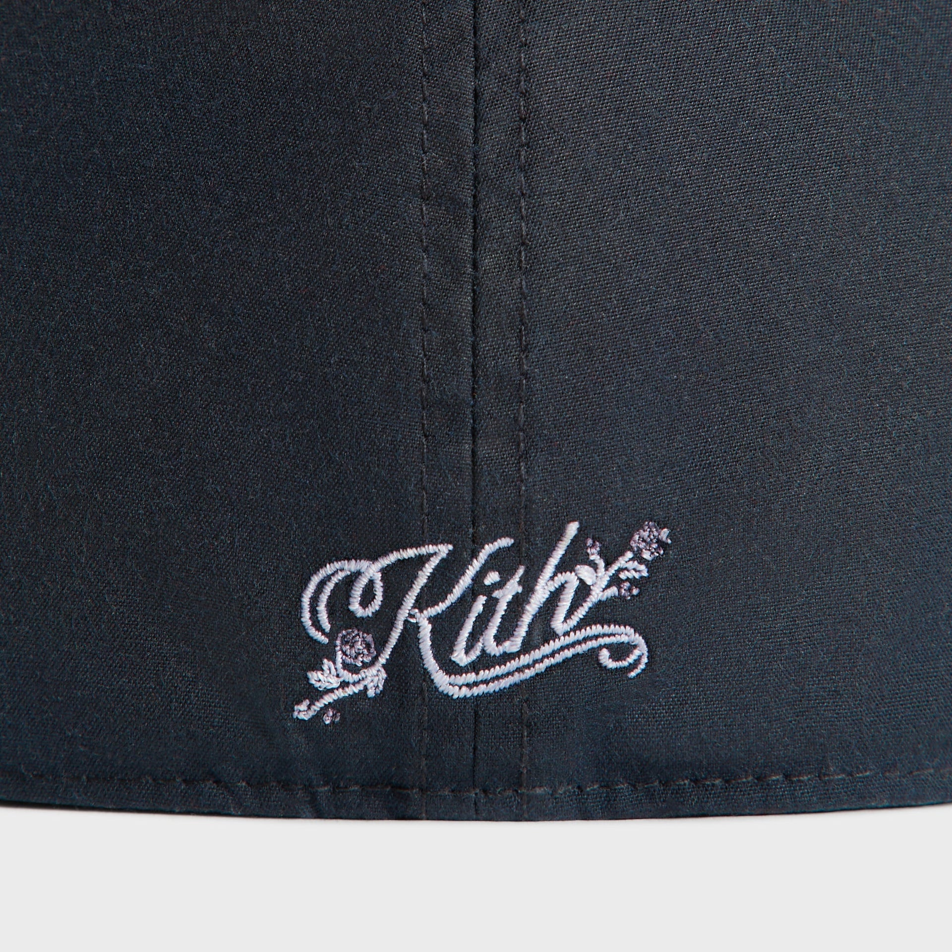 Detail of the white Kith script logo with roses on the rear of the nocturnal navy Yankees Franchise cap