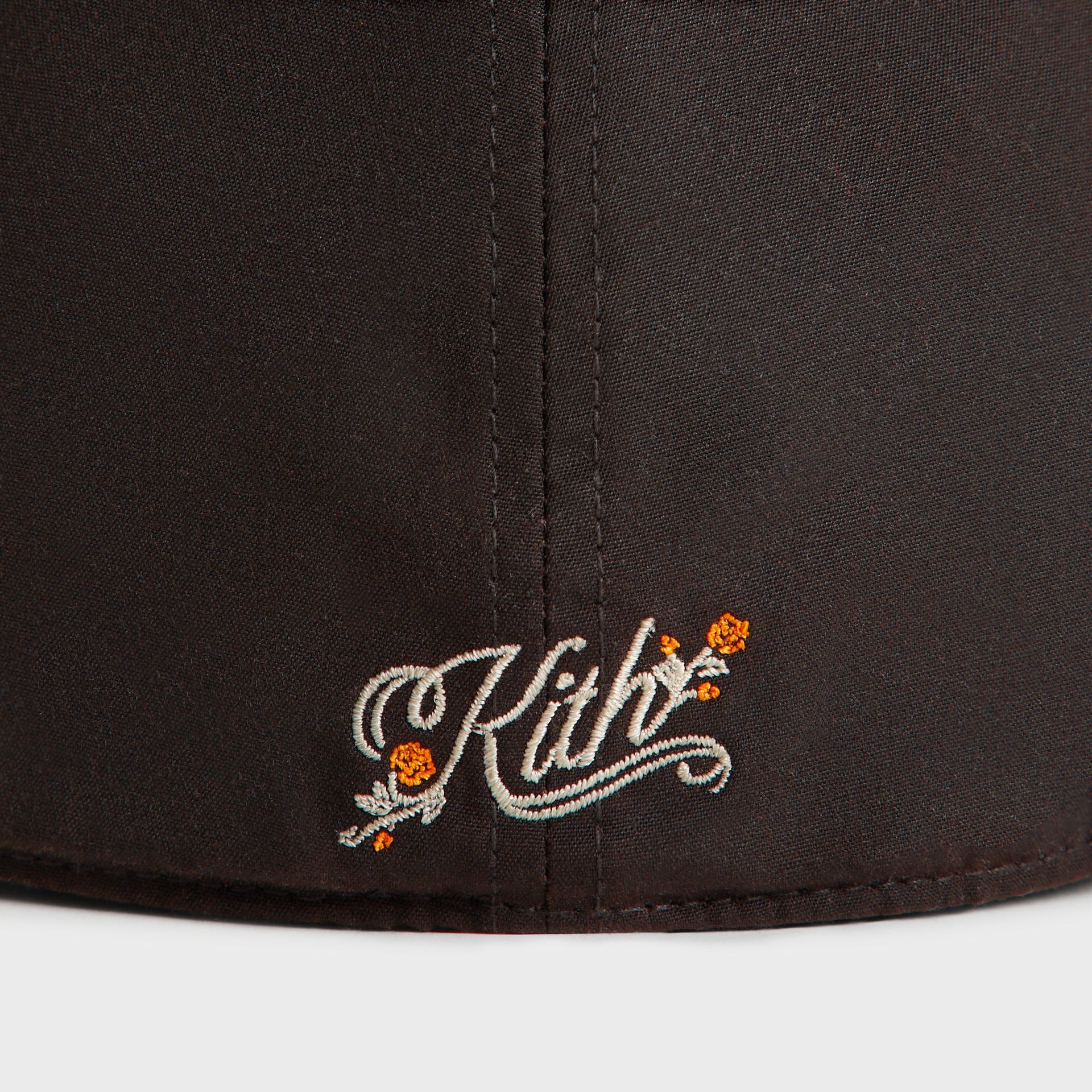 Close-up of the cream Kith rose-script with orange flowers on the back of the brown Kindling Mets cap.
