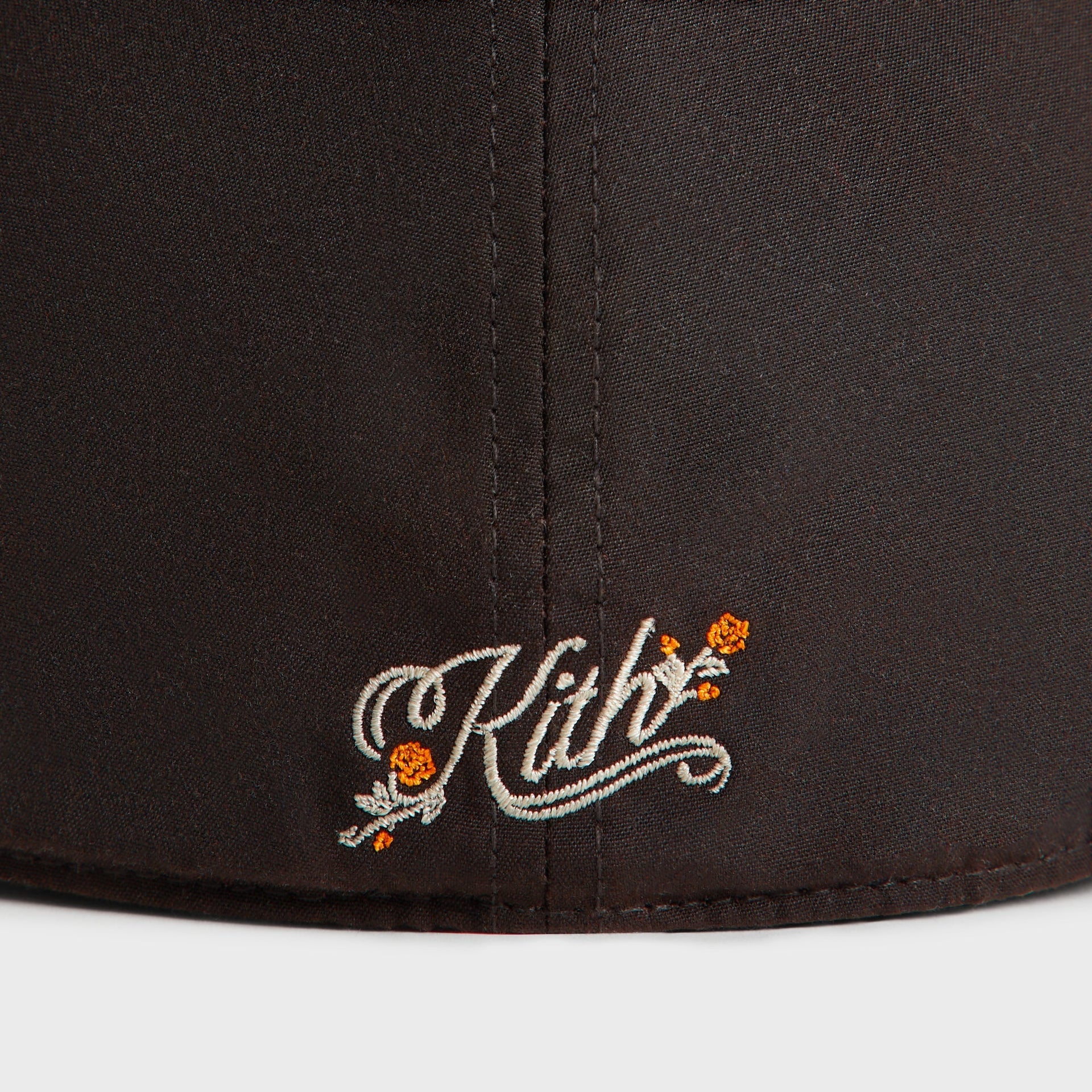 Detail of the cream Kith script logo with orange roses on the rear of the kindling brown Mets Franchise cap