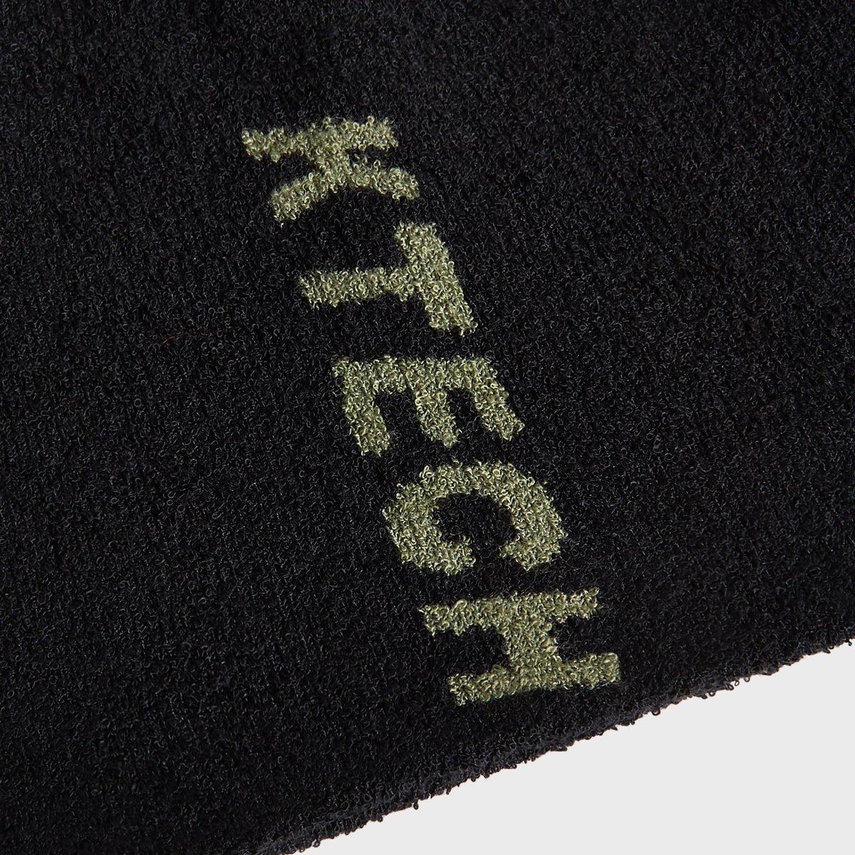 Close-up of embroidered olive KTECH logo on Kith Boucle Cuffless Beanie knit texture