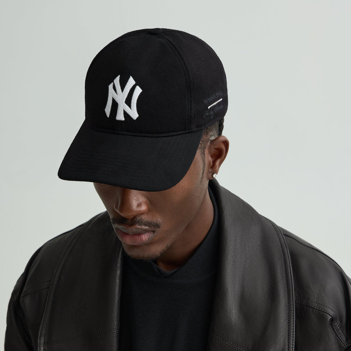 Model wearing the Giorgio Armani & Ronnie Fieg for '47 black wool fitted cap with NY logo, paired with a black leather jacket