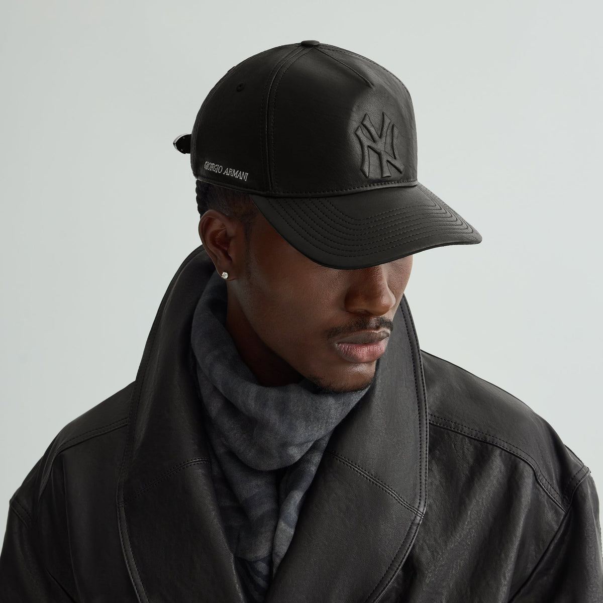 Model wearing the Giorgio Armani & Ronnie Fieg for '47 black soft leather Hitch cap with a black leather coat and gray scarf