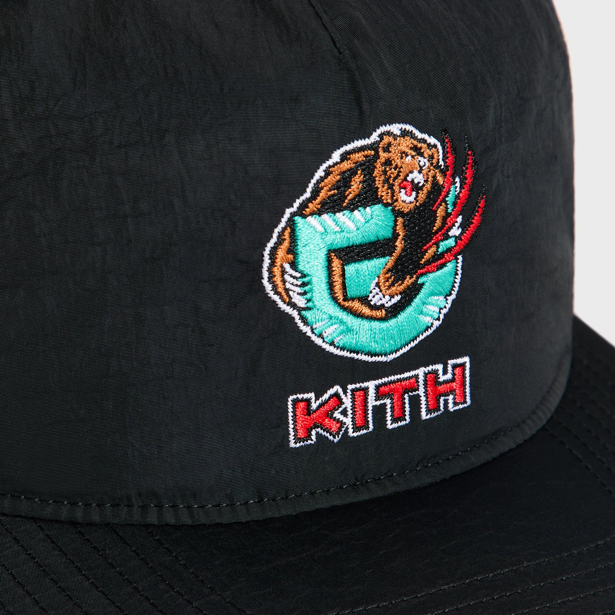Close-up of embroidered teal and brown Grizzlies bear logo with red Kith wordmark on black nylon snapback cap