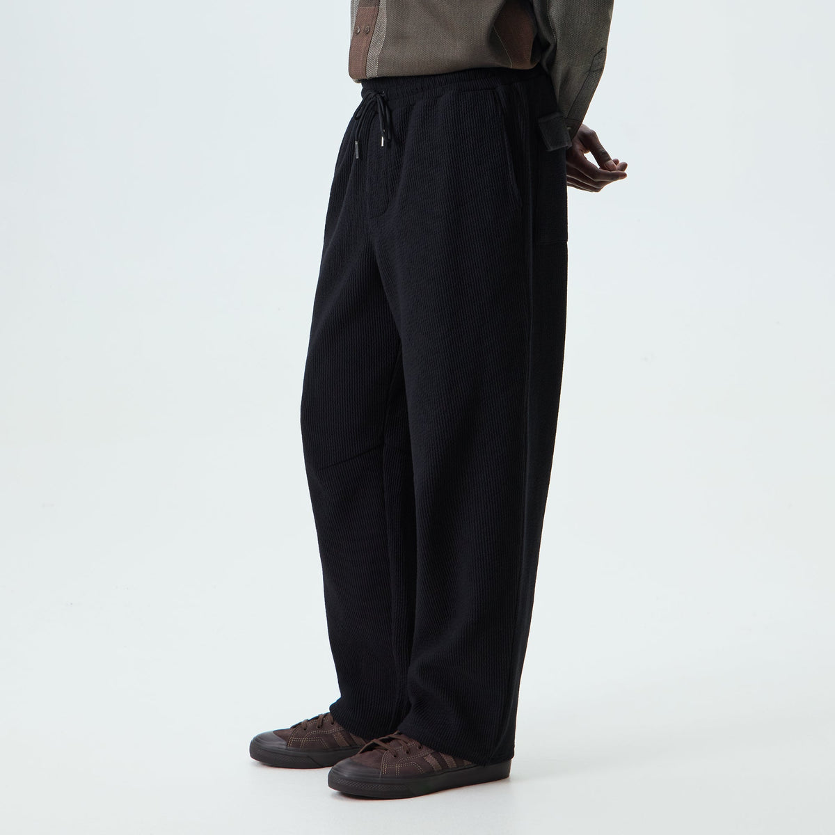 Kith Heavy Crepe Elmhurst Pant in black, on-model side view showing relaxed wide-leg fit and drawcord waist with brown sneakers