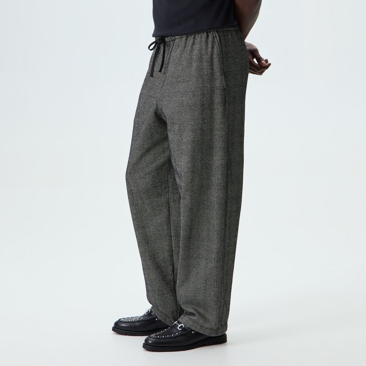 Man wearing black herringbone Kith Chenille Grayson trousers, side view