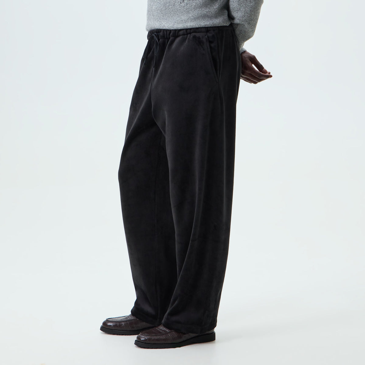 Man wearing black Kith Plush Double Fleece Grayson velour trousers, side view, with loafers