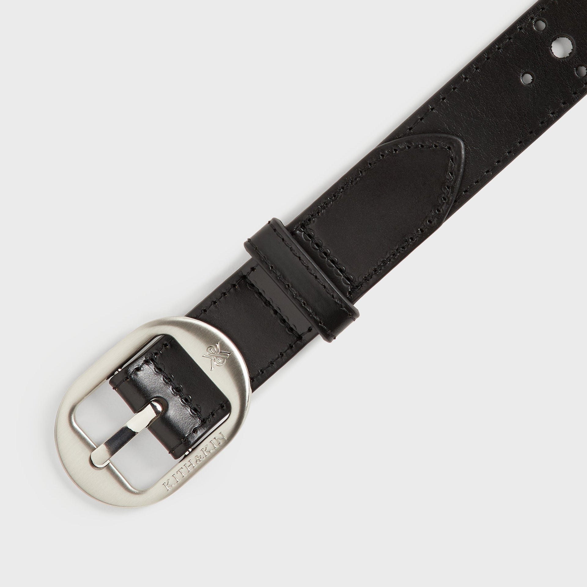 Kith Studded Leather Belt in Black, close-up angled view of the brushed silver oval buckle with engraved logo