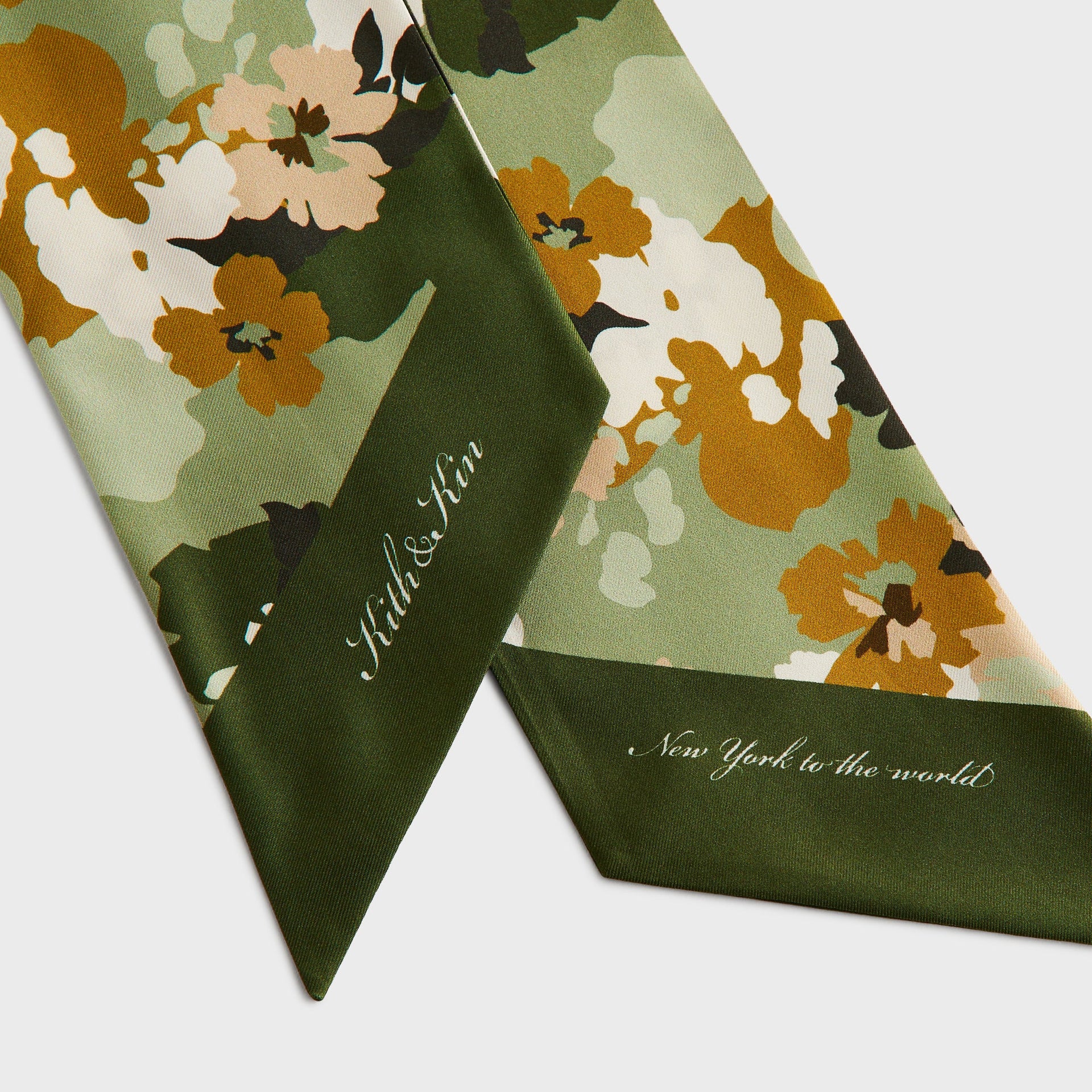 Close-up of the olive green tips on Kith Printed Silk Neck Tie in Sage reading Kith & Kin and New York to the World