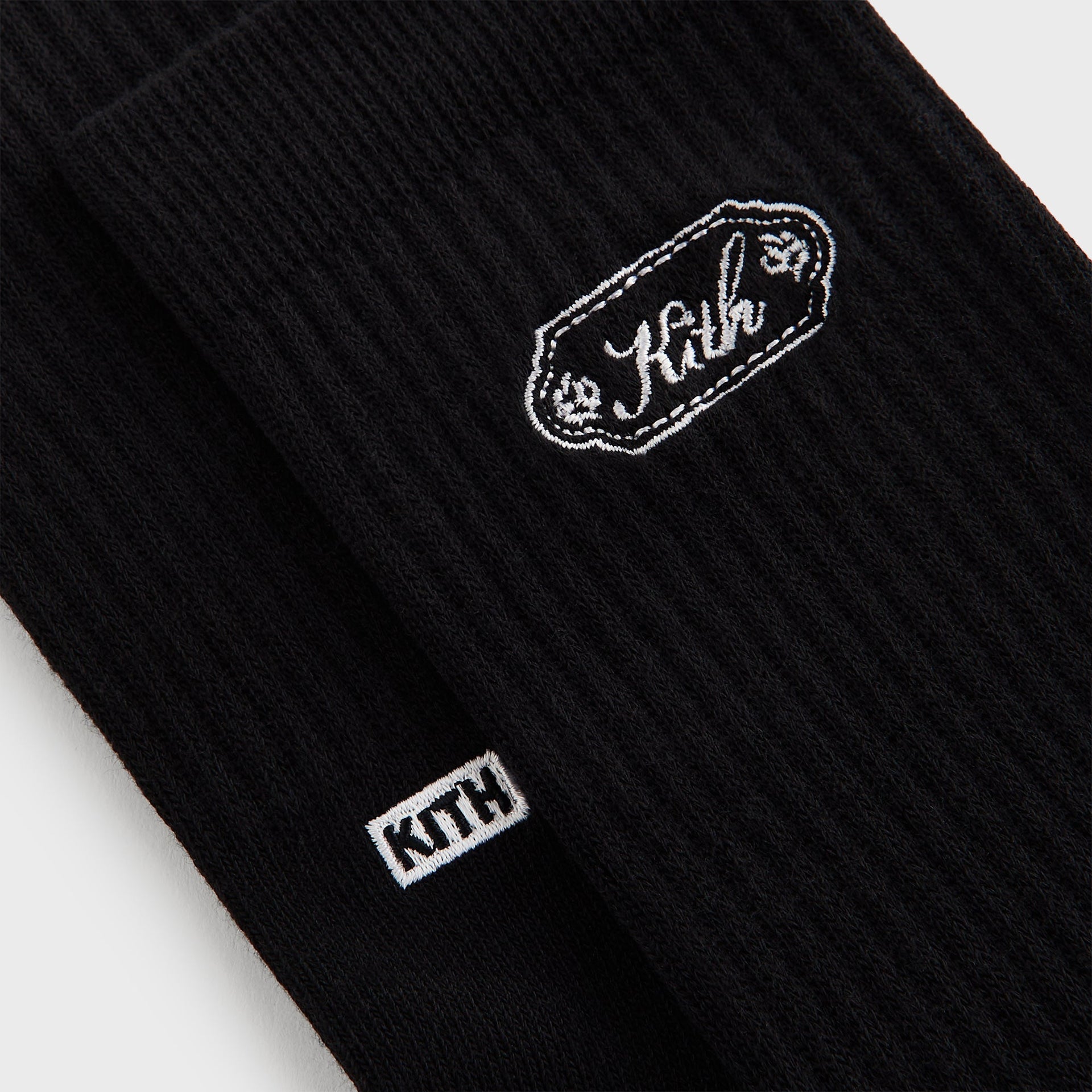 Close-up of the black crew sock featuring the Kith script plaque patch with floral embroidery accents