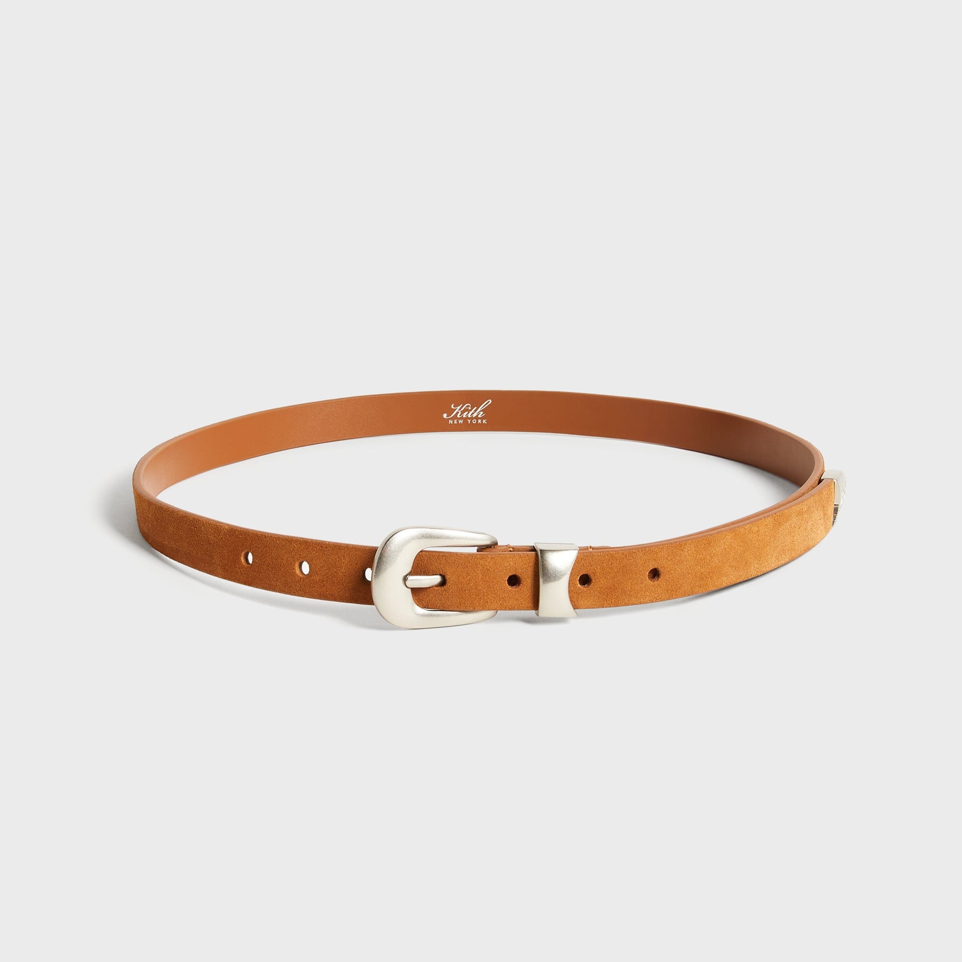 Kith Western Suede Belt in Argil tan, coiled view showing the western-style silver buckle and Kith New York branded leather backing