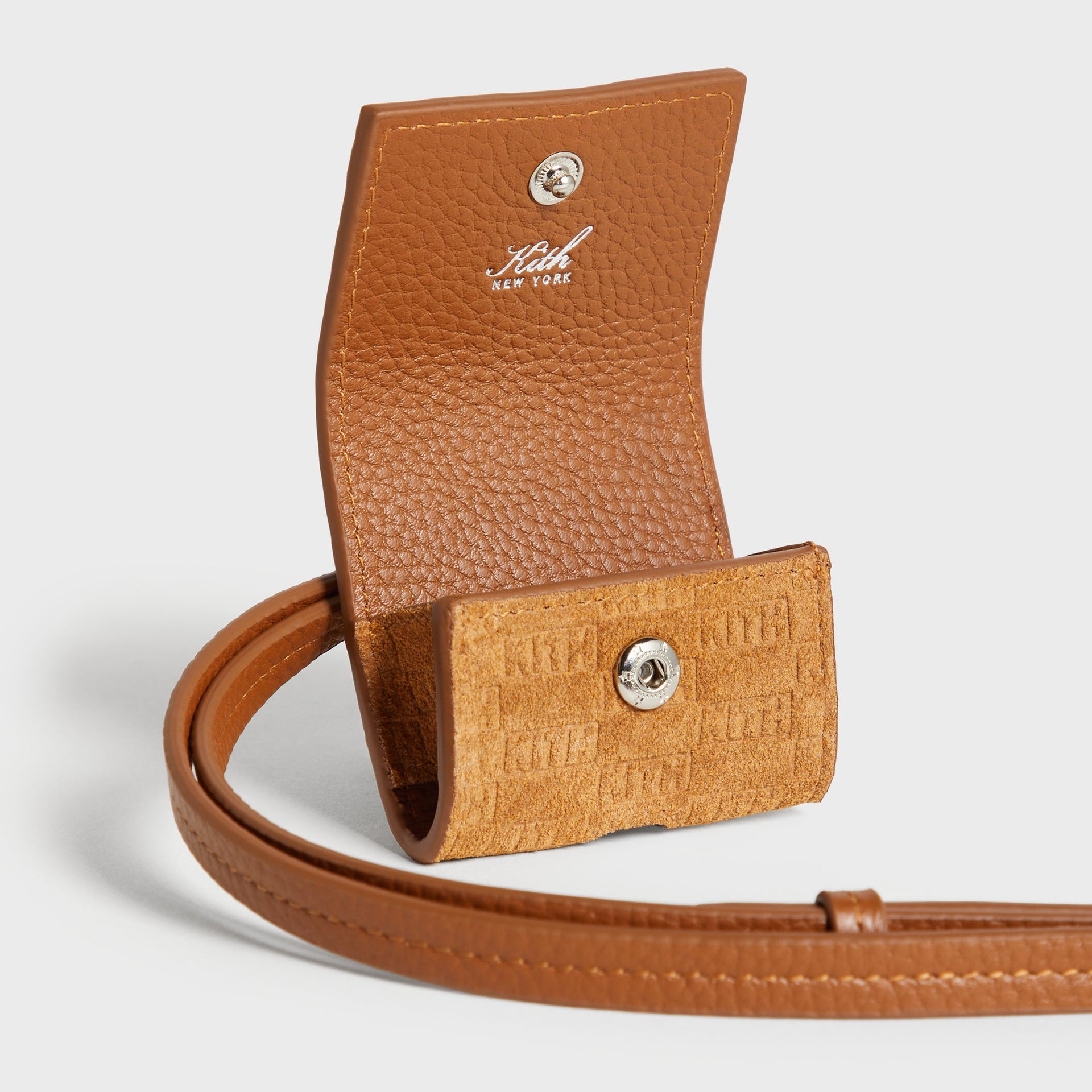 Close-up of the Kith Monogram Suede AirPod Case in tan showing the open flap with Kith New York logo stamp and the snap-button suede pouch