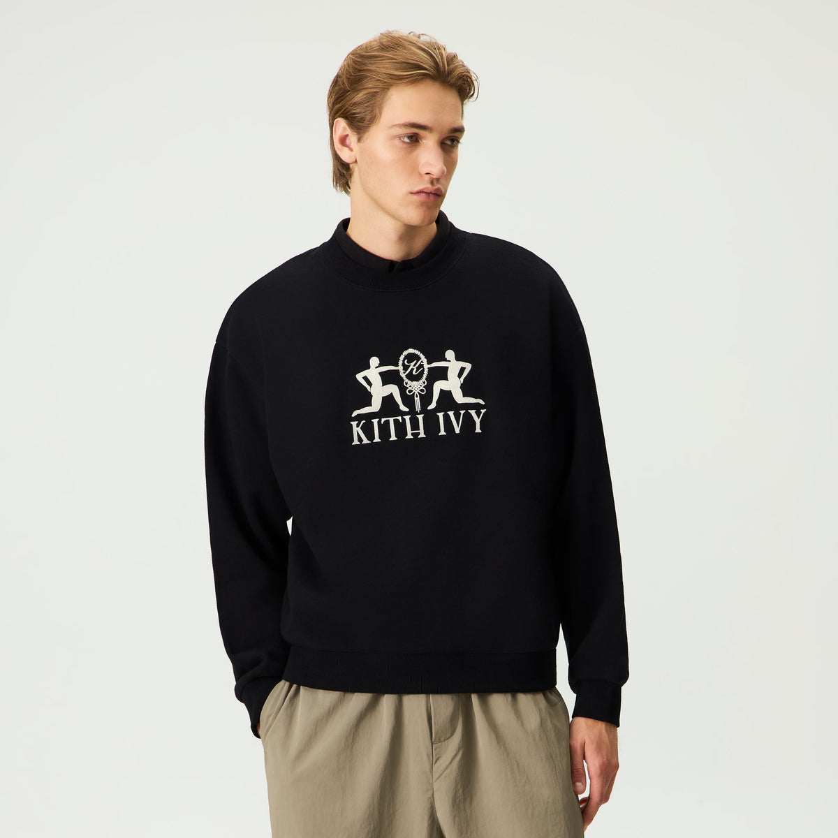 Model wearing black Kith Ivy Emblem Vintage Crewneck with embroidered chest emblem and khaki pants, front view