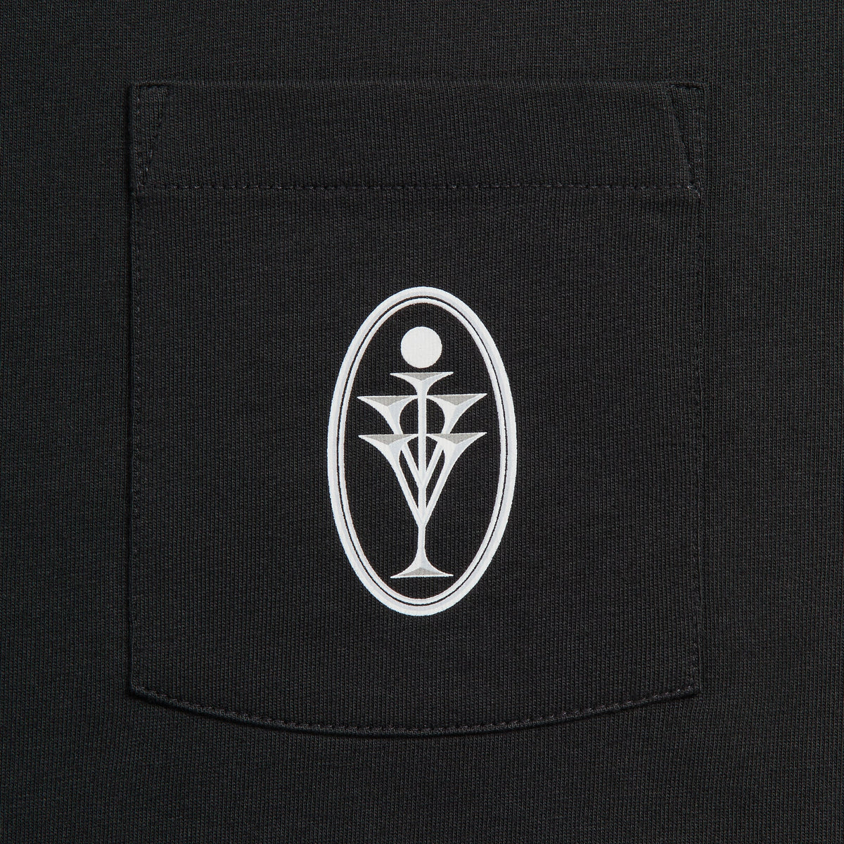 Close-up of white oval goblet emblem on chest pocket of black Kith Ivy for Cafe Mogador Pocket Tee