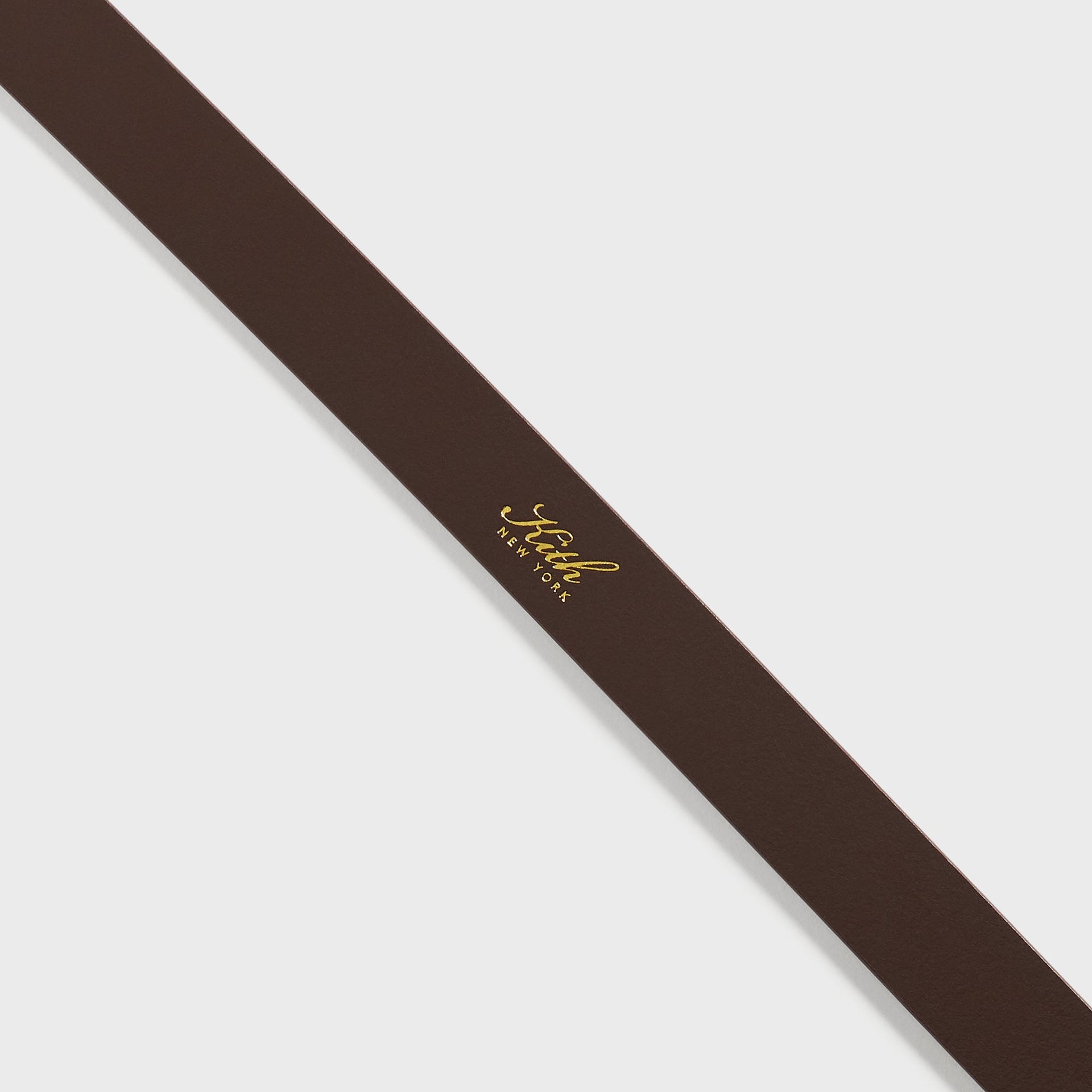 Detail of the Kith New York gold foil logo stamped on the Walnut leather strap of the Plaque Belt