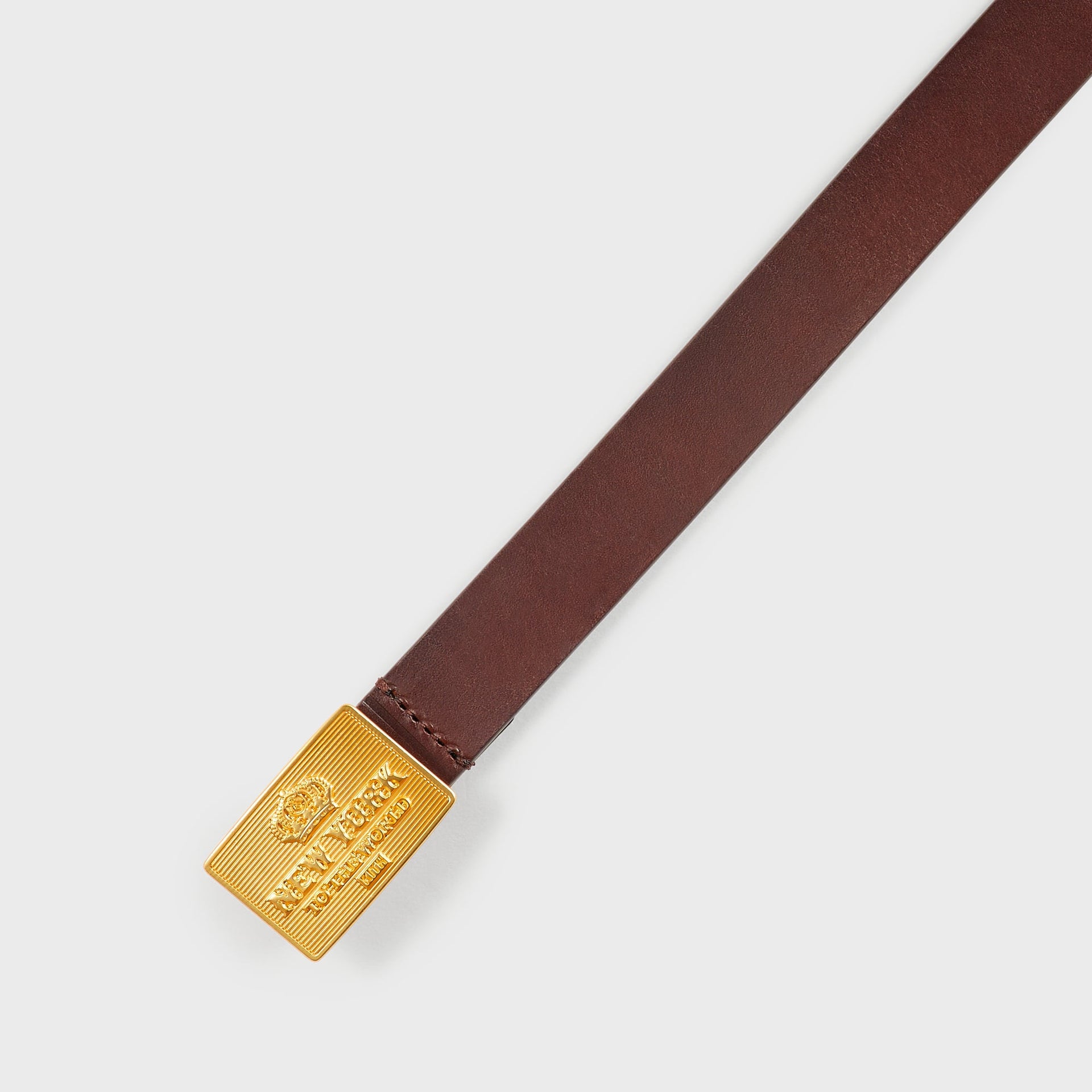 Close-up of the gold-tone rectangular buckle engraved New York to the World on the Kith Plaque Belt in Walnut