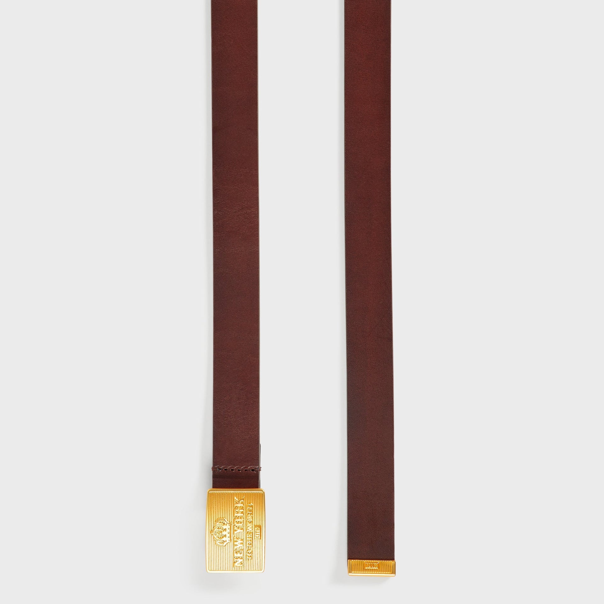 Both ends of the Kith New York Plaque Belt in Walnut, showing the gold buckle and leather keeper loop tip