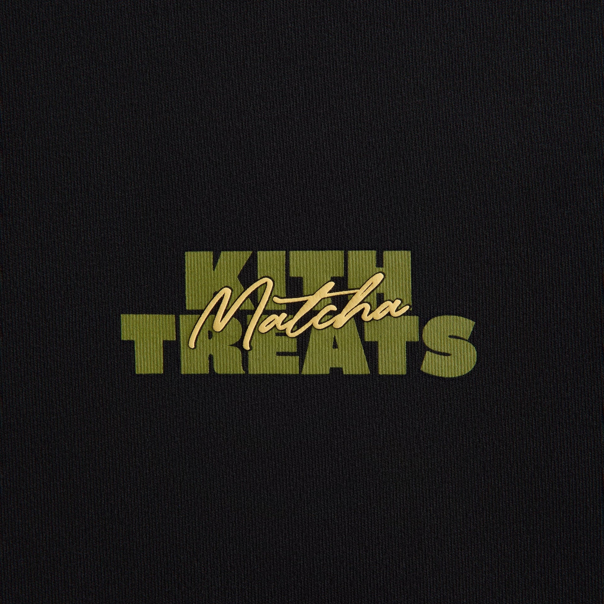Close-up of Poster Tee front print: green Kith Treats lettering with gold Matcha script on black cotton