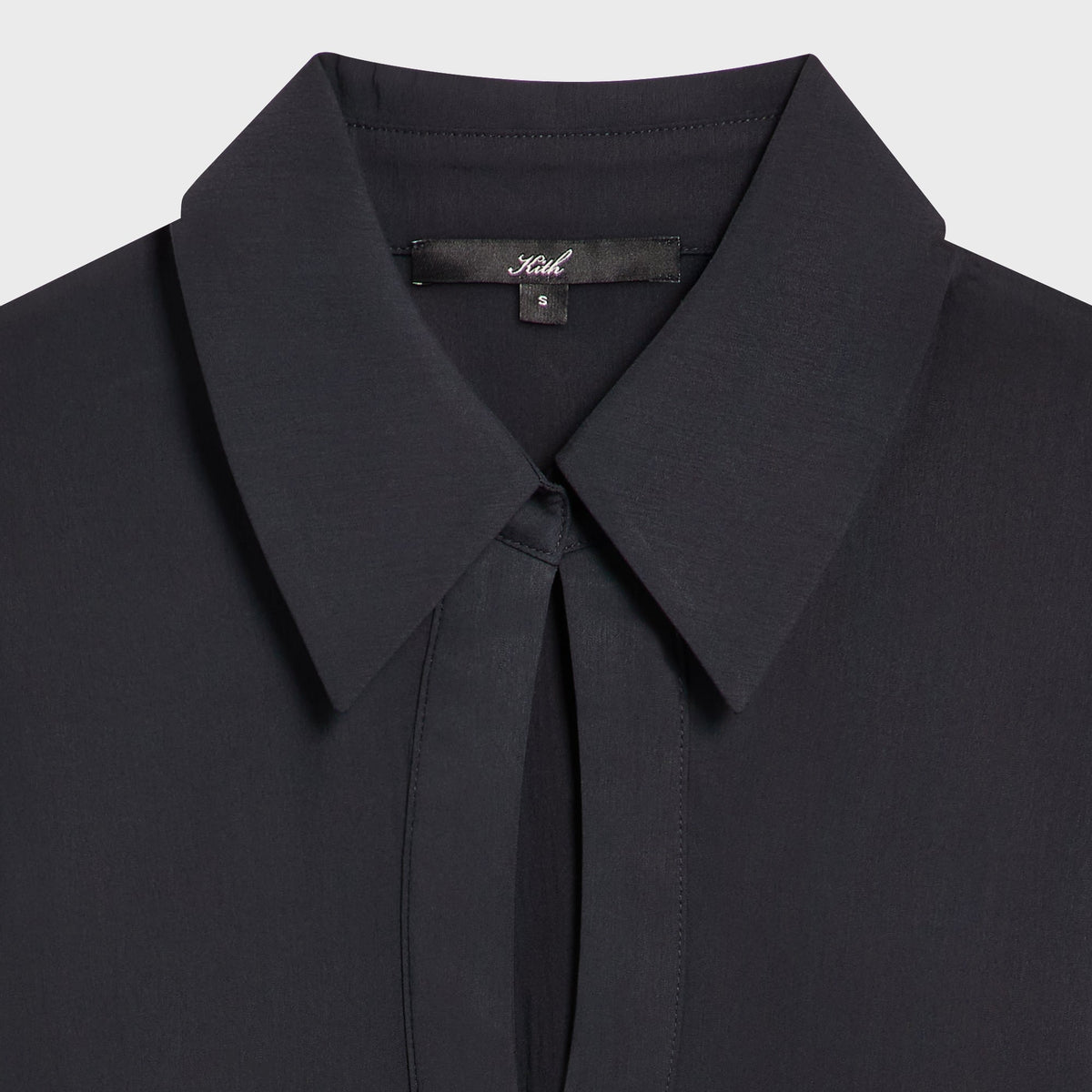 Close-up of the plunge keyhole collar and Kith label on the Camilla plunge shirt in black