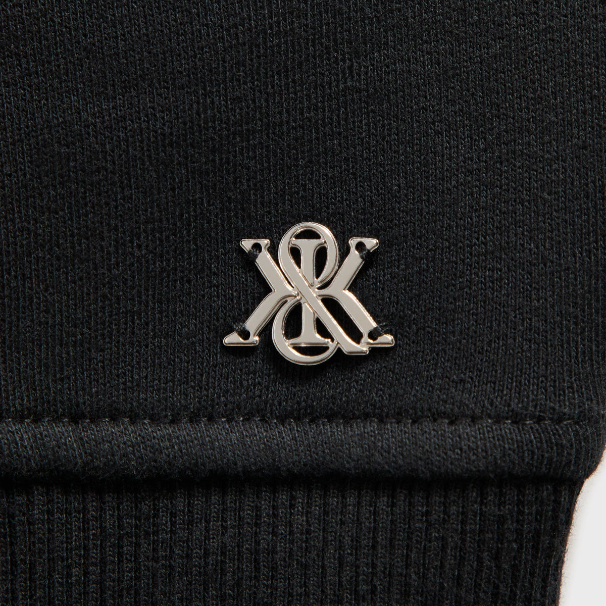 Close-up of the metal K charm hardware on the Kith Evie moto paneled jacket in black