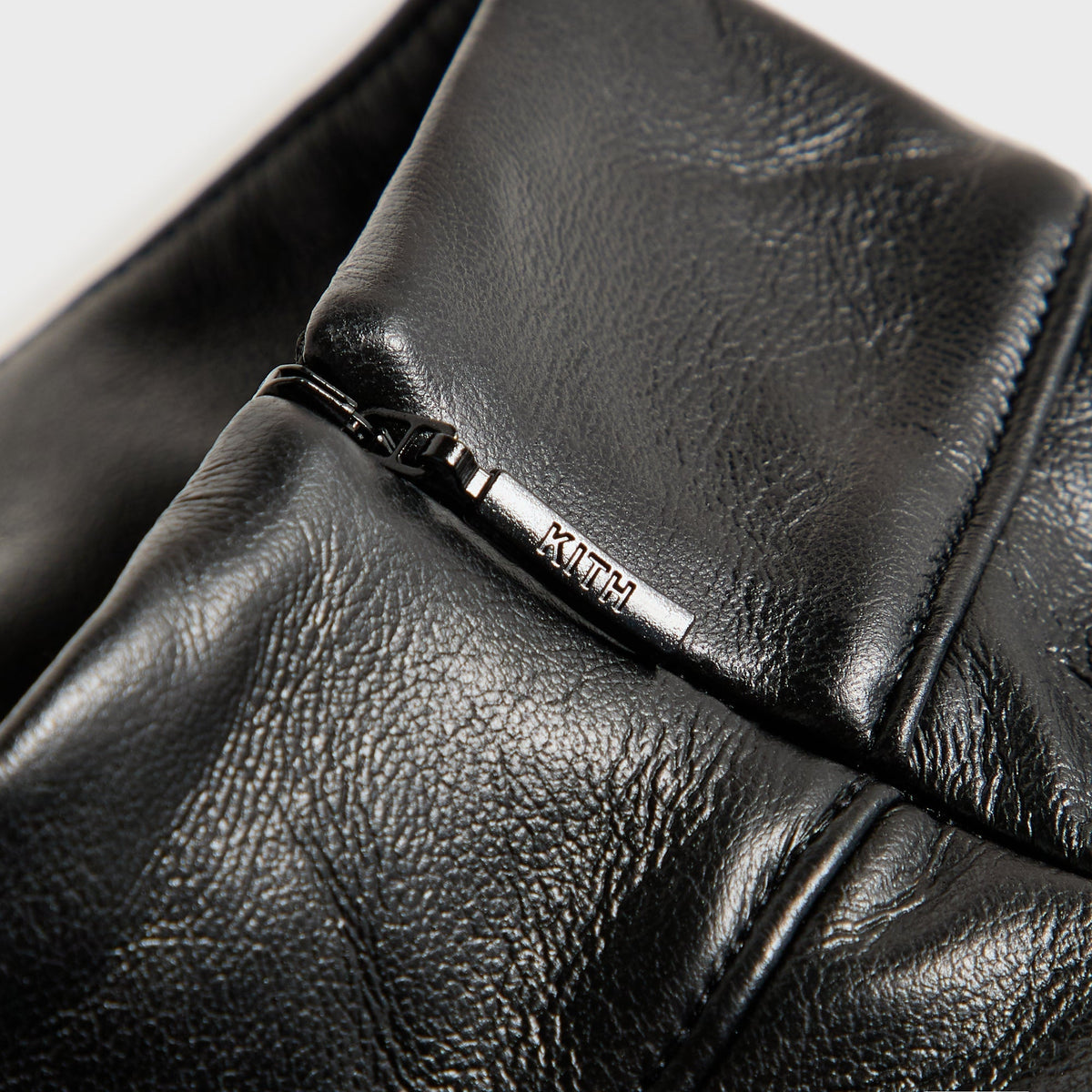 Close-up of the zipper pull engraved with the Kith logo on the Duri faux leather top