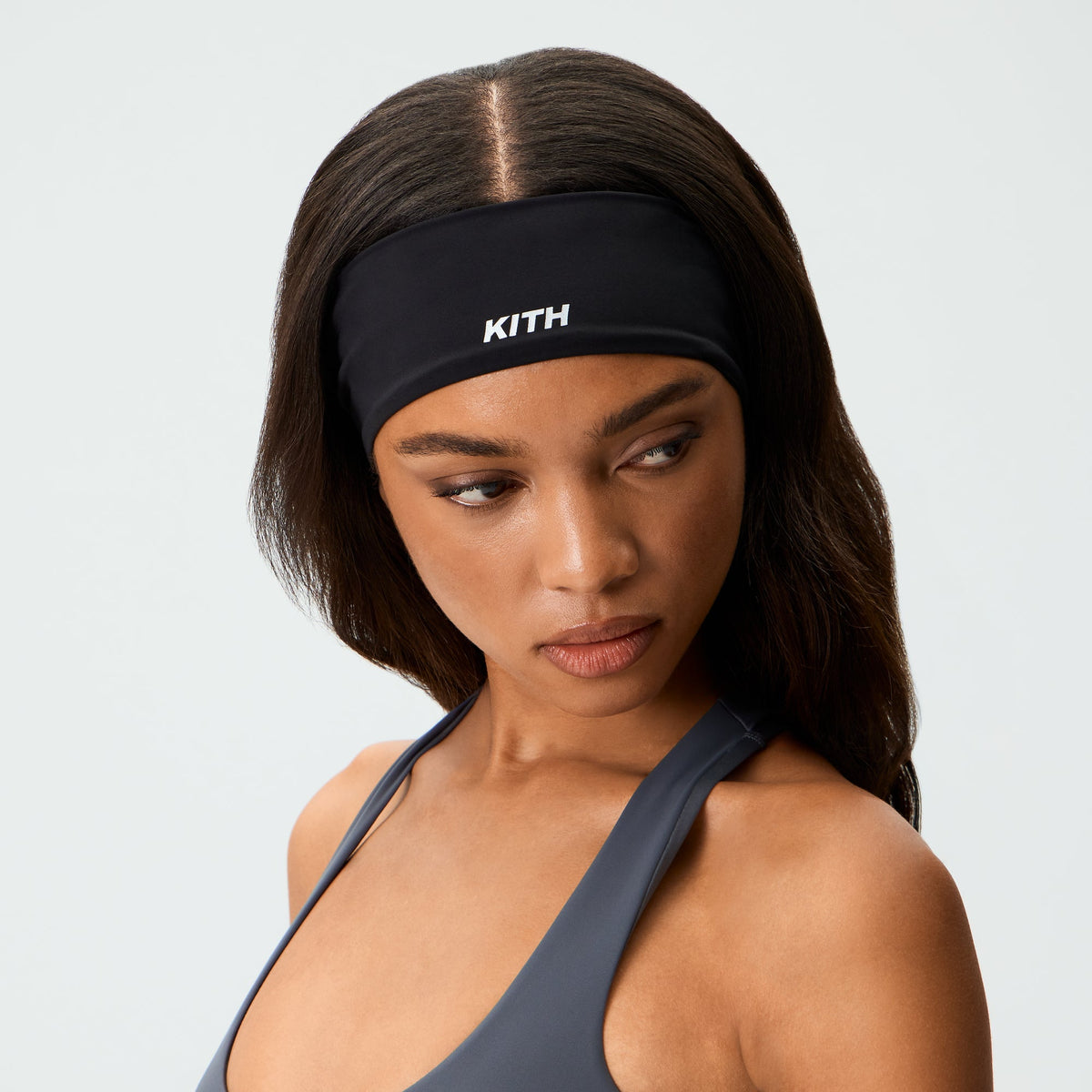 Woman wearing Kith Women's Active Headband in black over dark hair, close-up portrait