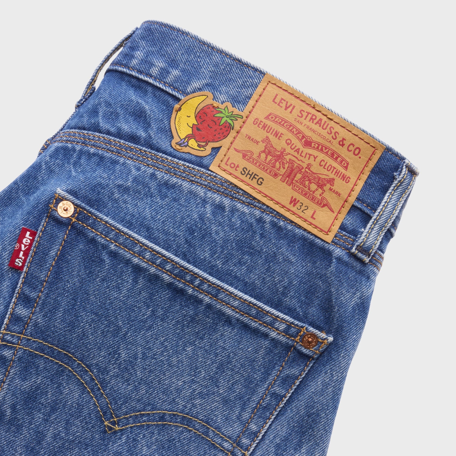 Close-up of Levi's x Sky High Farm denim shorts back waist: leather 'SHFG' patch, banana-and-strawberry mascot decal and red Levi's tab