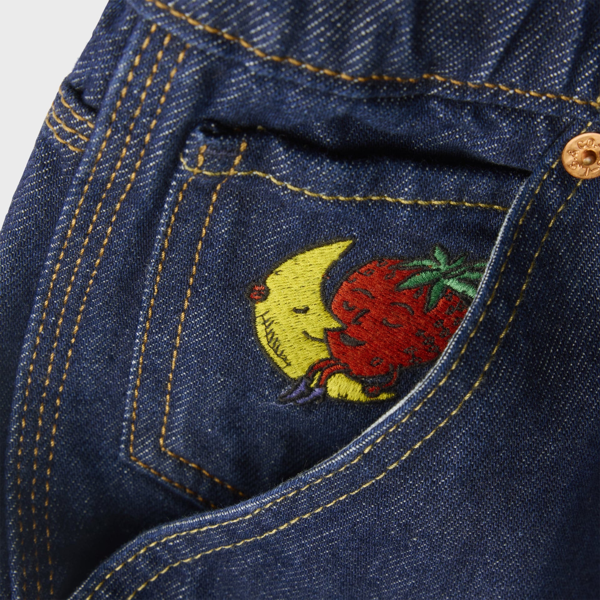 Close-up of Levi's x Sky High Farm mid-indigo overalls back pocket with embroidered smiling moon and strawberry mascot