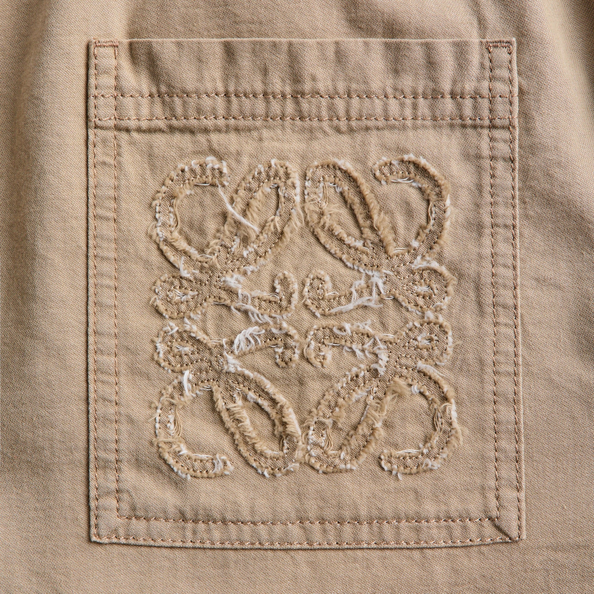 Close-up of frayed tonal Anagram appliqué on the beige cotton shorts back pocket