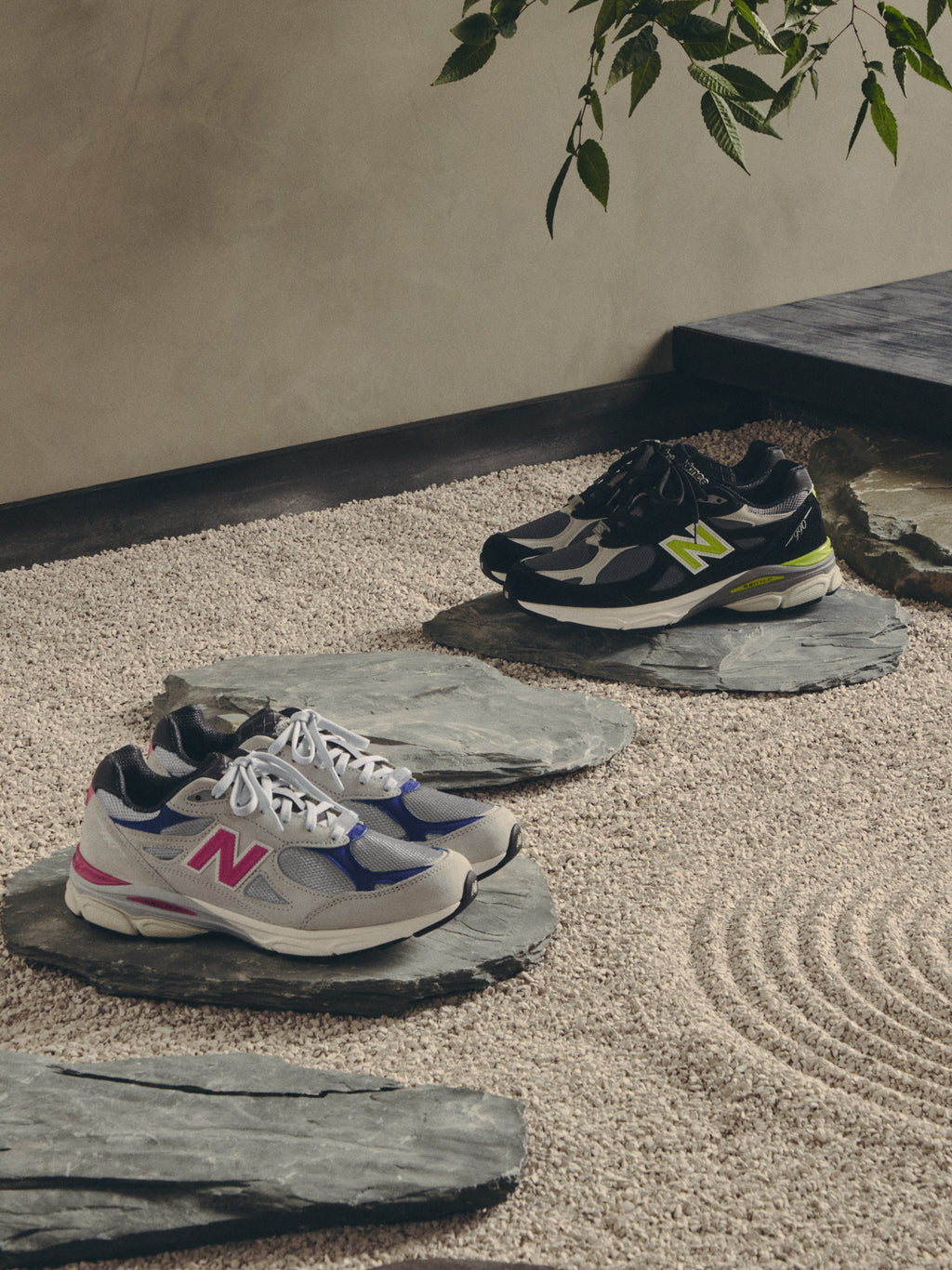 Cream and black Kith x New Balance 990 pairs on slate stepping stones in a zen garden, wide mobile banner crop