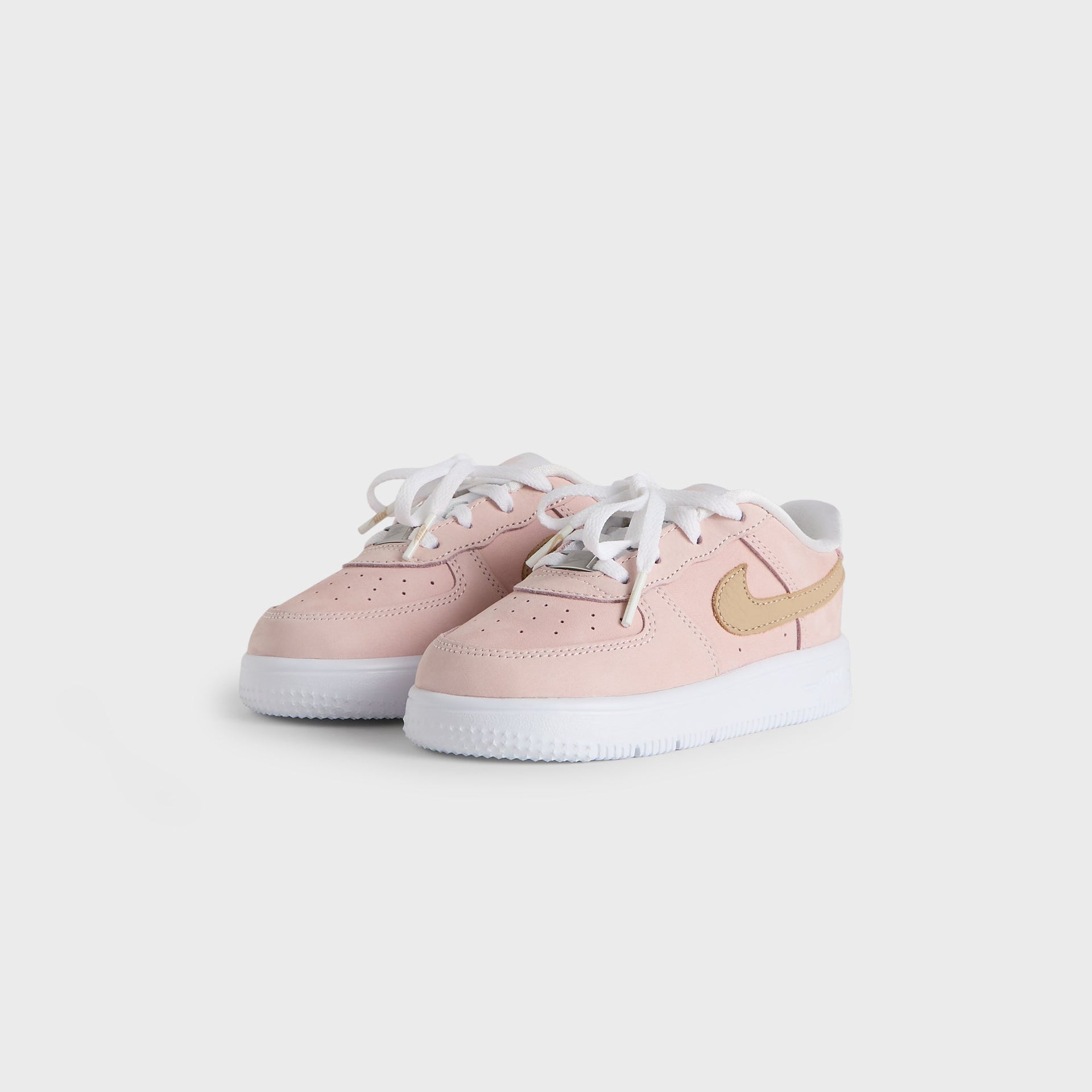 Kith Kids x Nike TD Air Force 1 Un-Linen in pink, angled front three-quarter view of the pair with white laces and wheat Swoosh