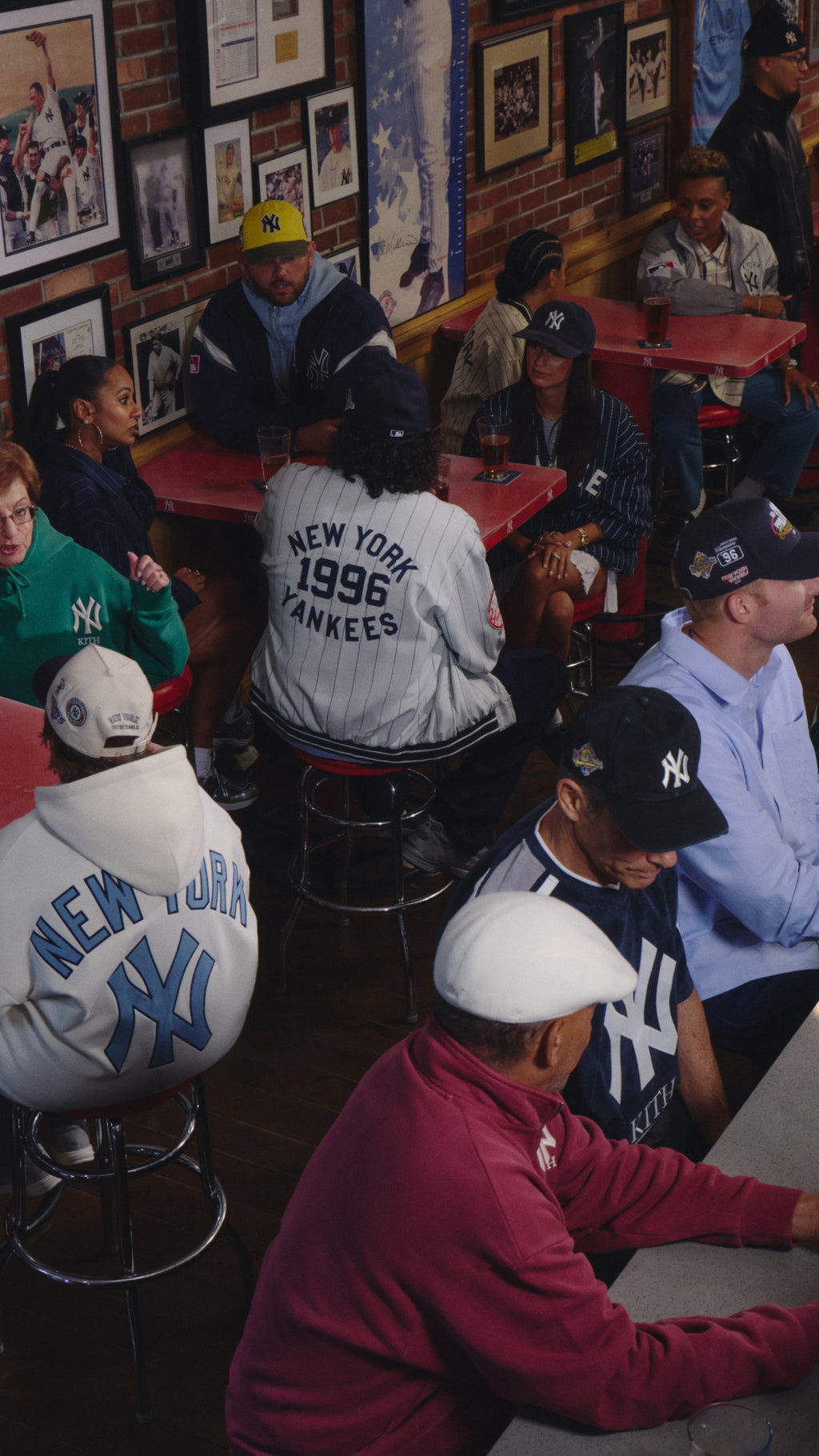Kith for New York Yankees campaign, mobile crop: fans in Kith x Yankees hoodies, jerseys, and caps gathered at bar tables lined with memorabilia