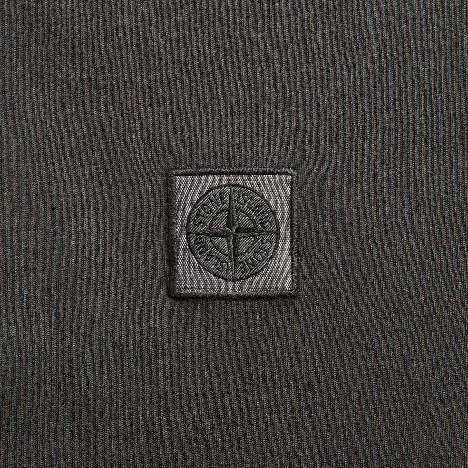Stone Island charcoal tee, close-up of woven square compass-rose logo patch on cotton jersey