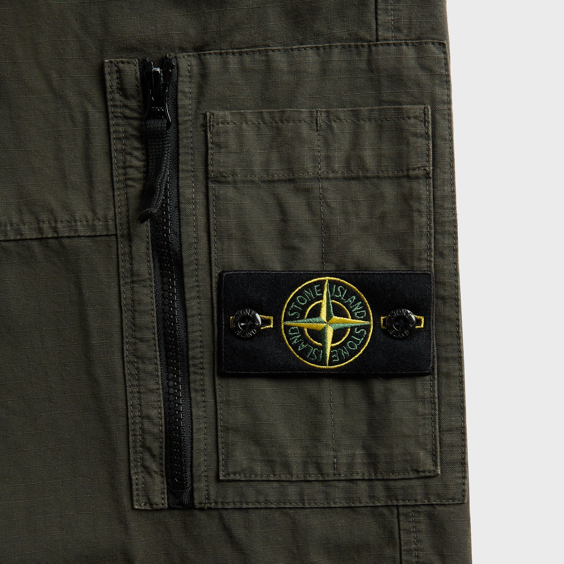 Detail of zip cargo pocket with Stone Island green and yellow compass badge on coal grey trouser