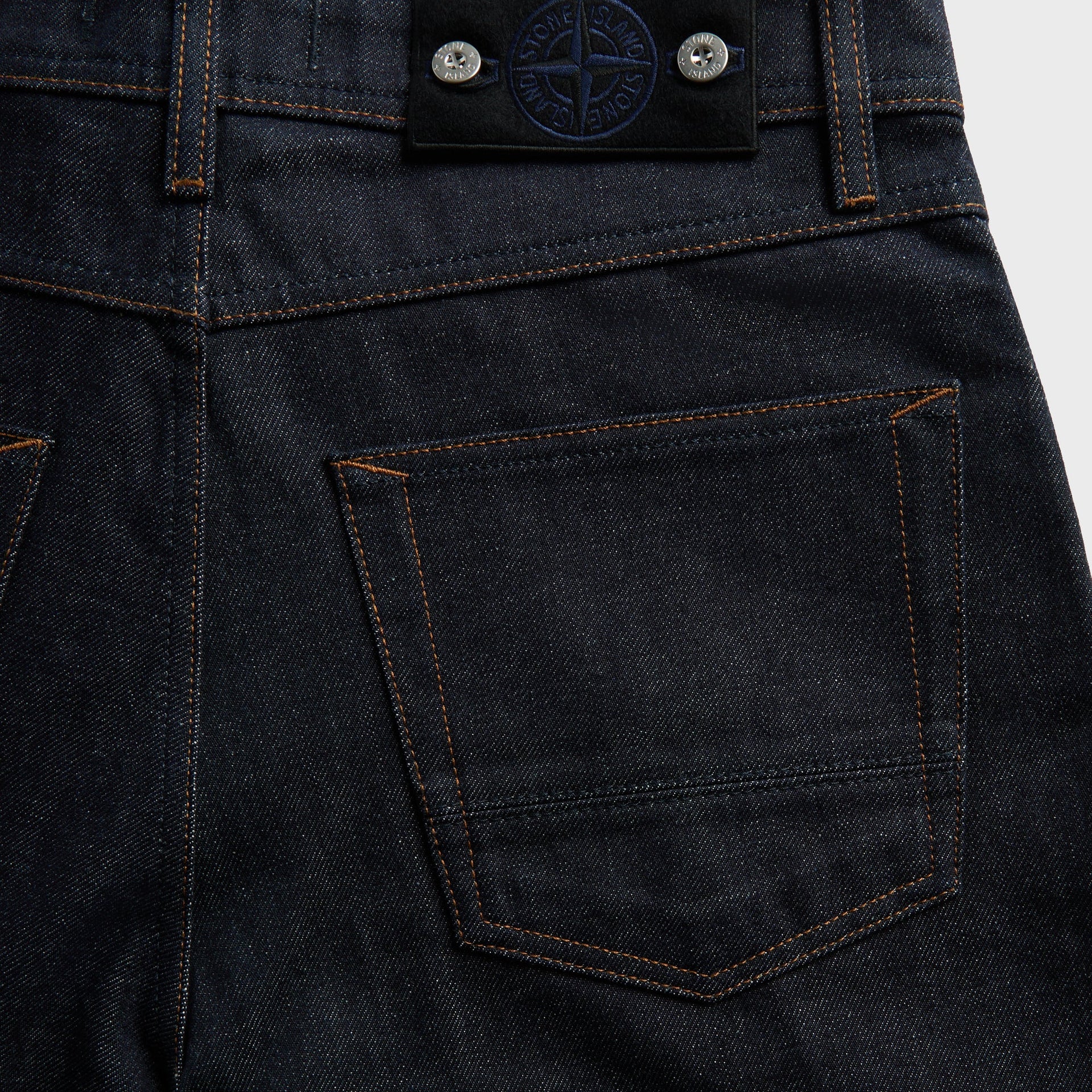 Detail of Stone Island leather compass tab and back pocket contrast stitching on raw indigo denim