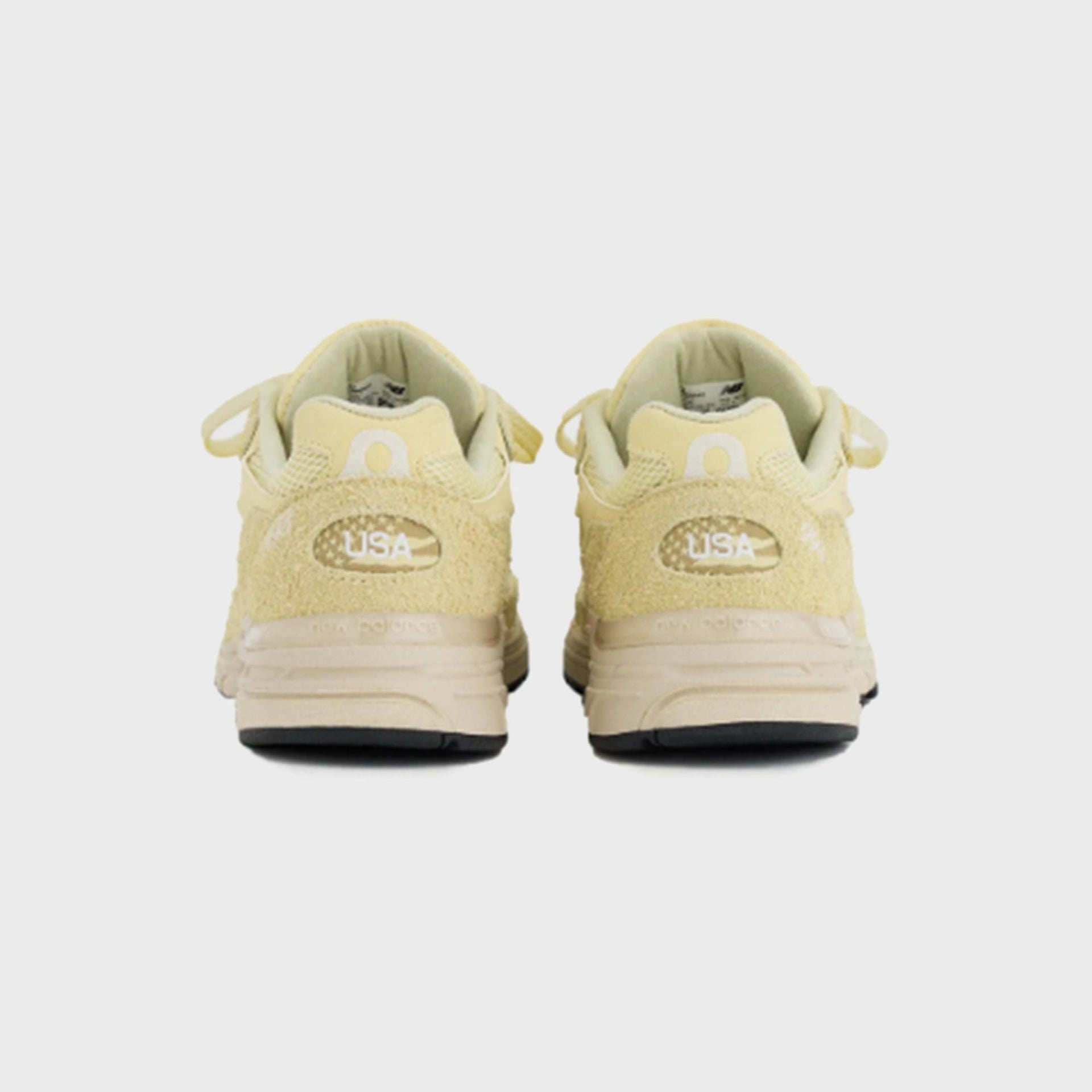 New Balance 993 Made in USA sneaker in pale yellow suede, rear heel view of pair showing USA flag patch